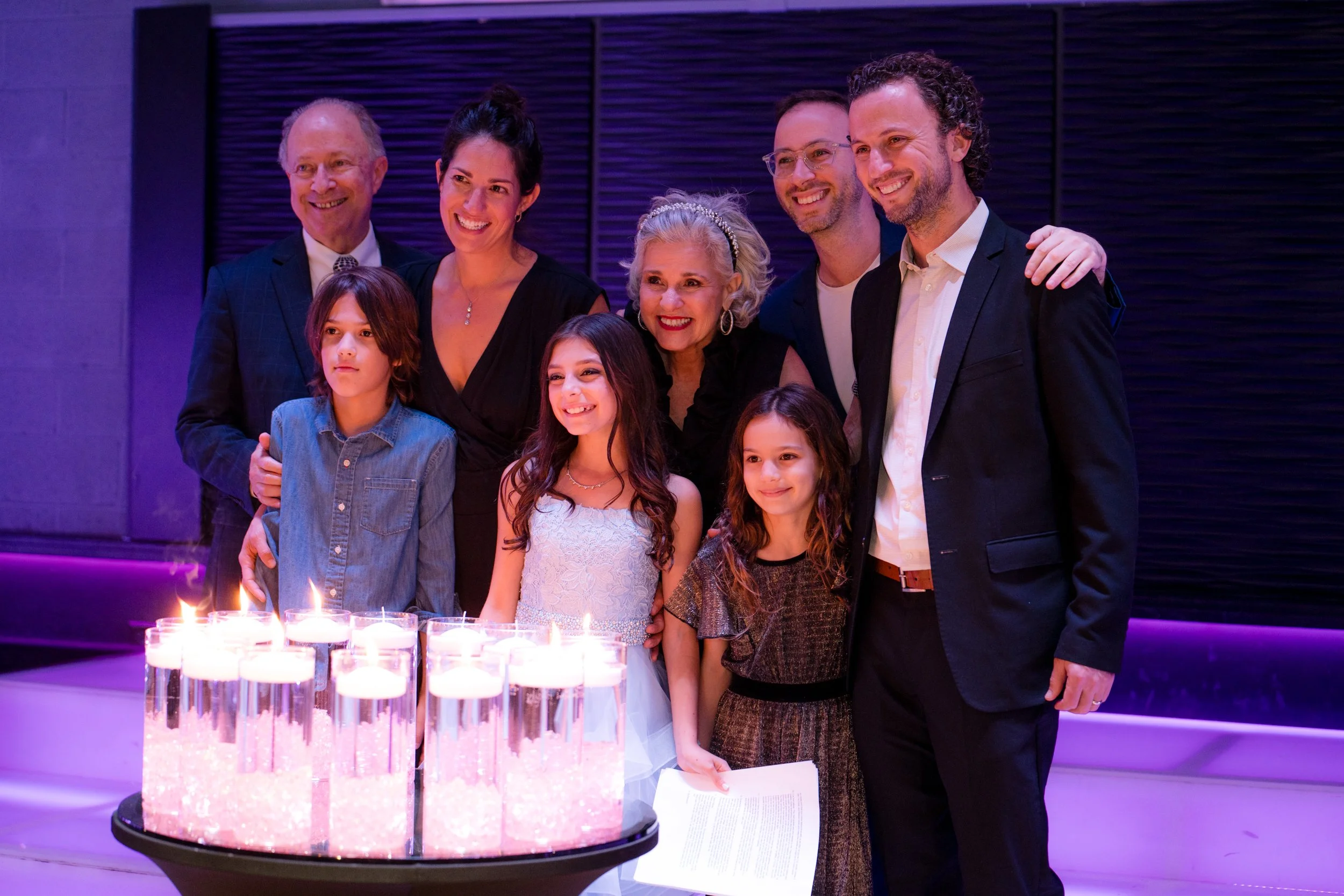A group of people, including adults and children, posing in front of floating candles during a celebration or event.