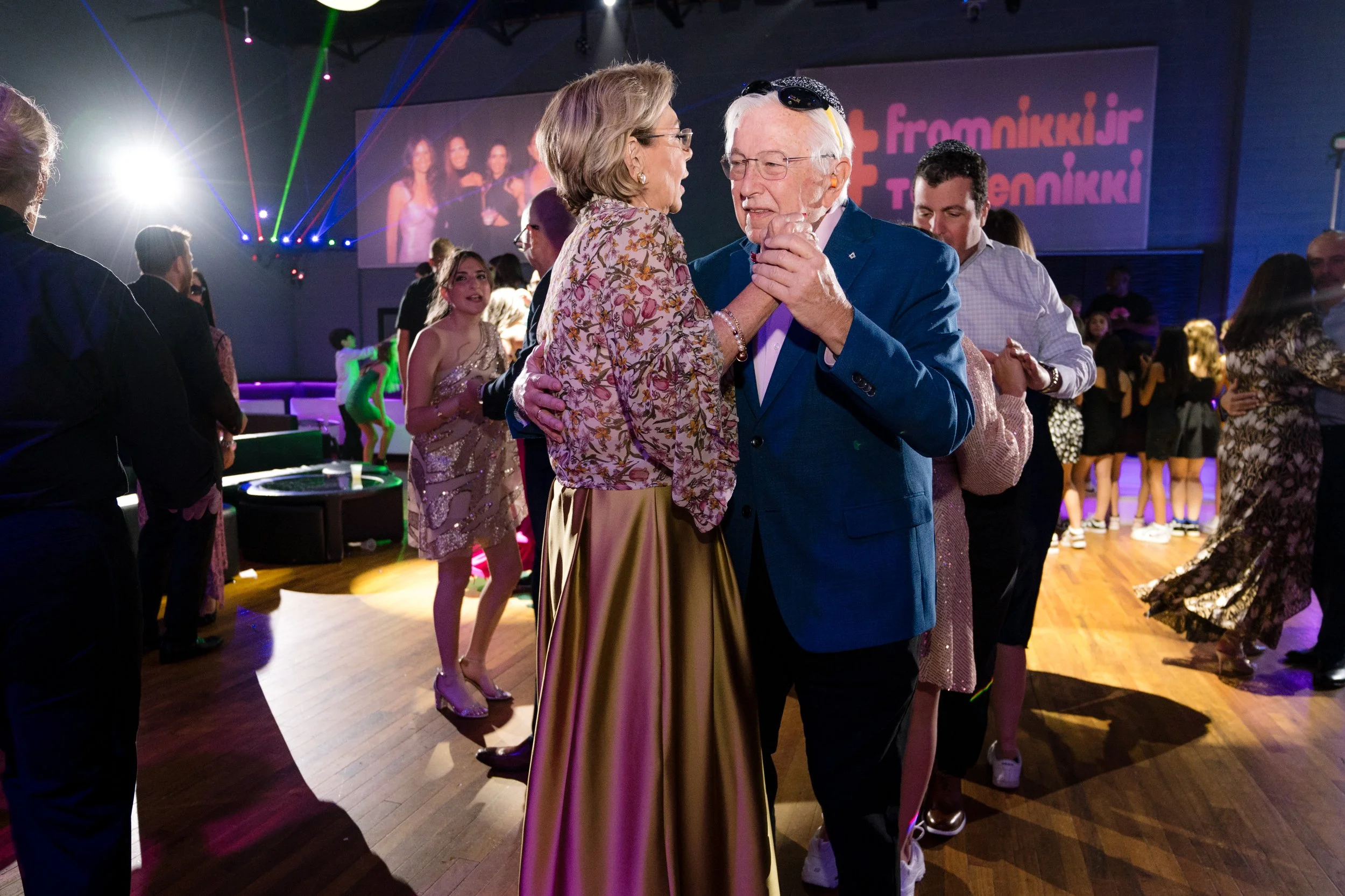 People dancing at a party with colorful lights and a projected image in the background.