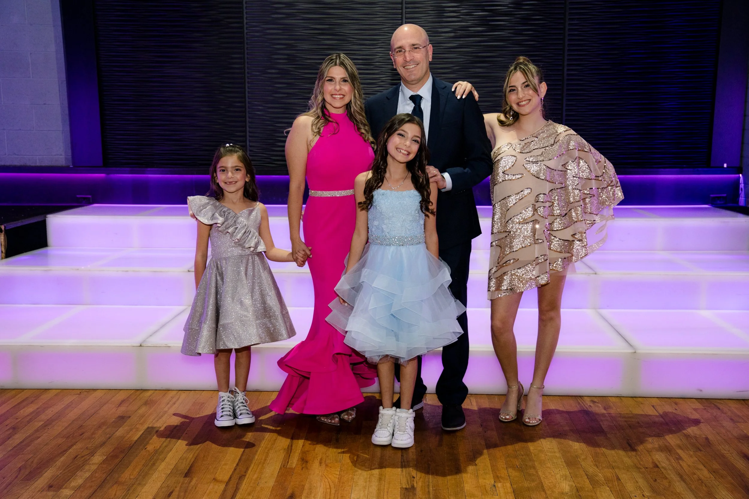 A family dressed in formal attire standing together on a lit stage with a wooden floor.