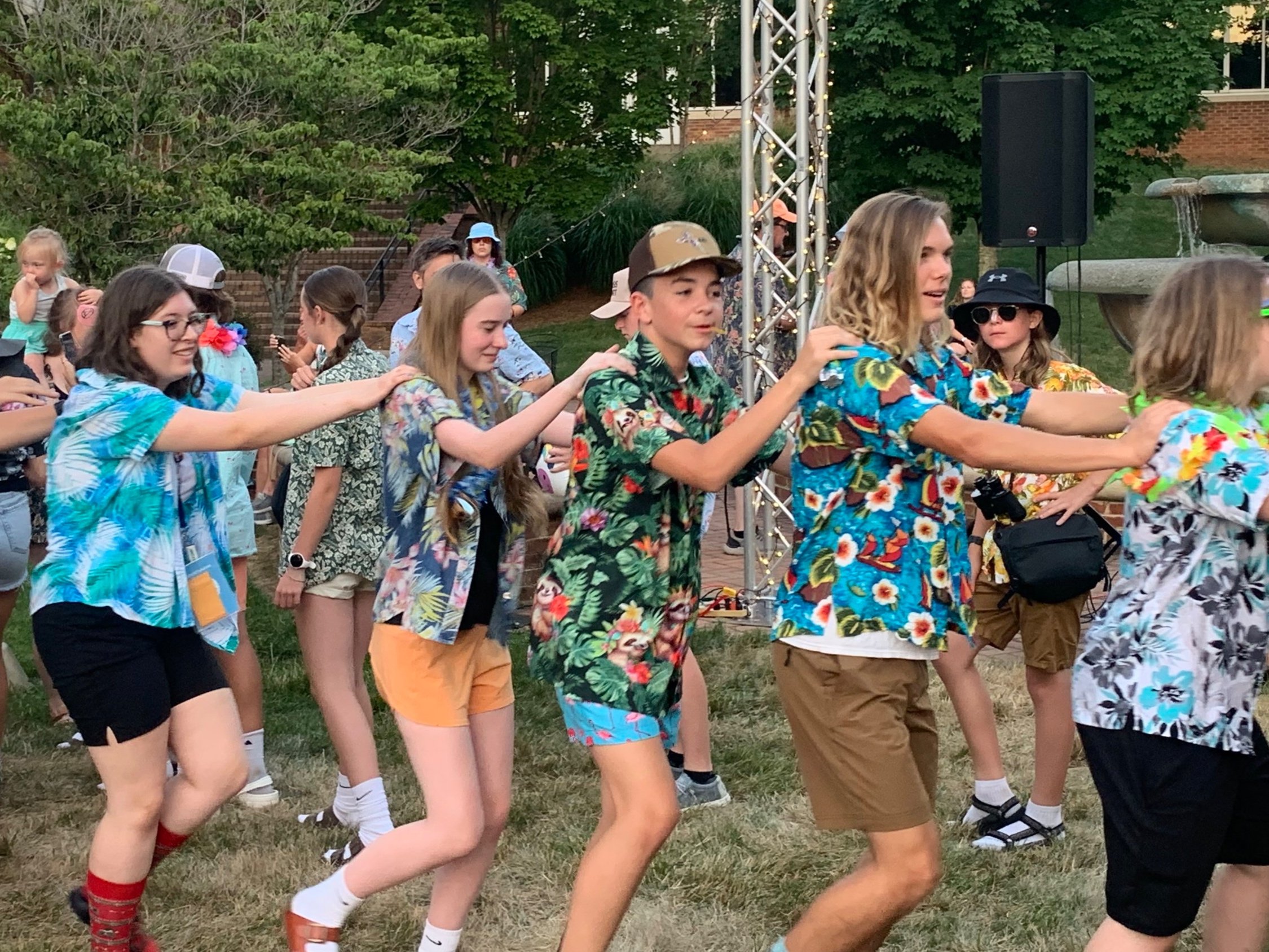 Group of people wearing Hawaiian shirts in a conga line outdoors.