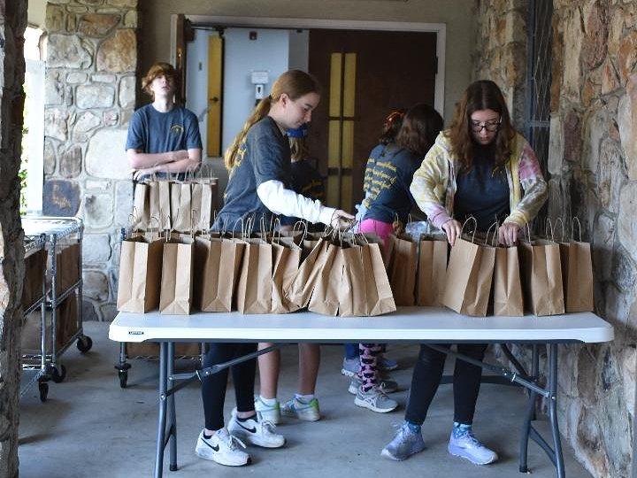 Group of people organizing brown paper bags on a table in an outdoor setting, possibly for a community or charity event.