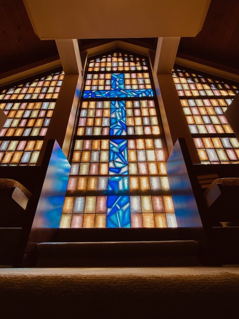 Colorful stained glass windows with a prominent blue cross design in a church setting.