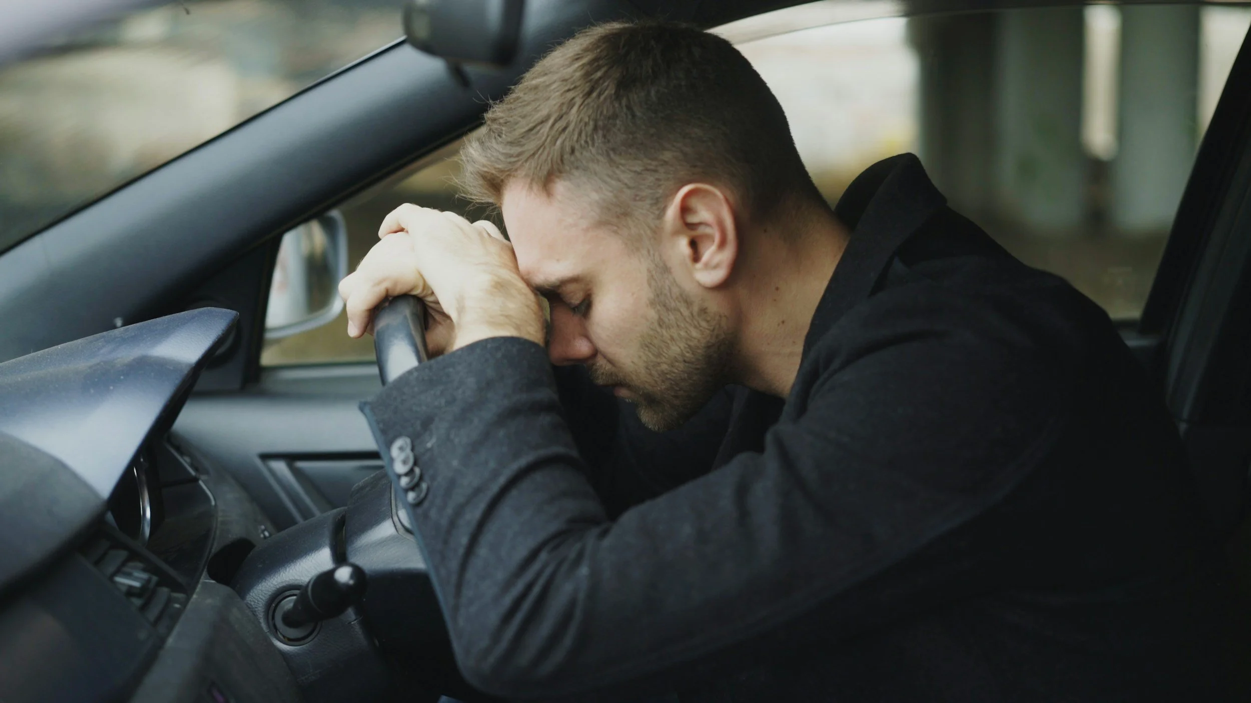 Man resting head on steering wheel in car