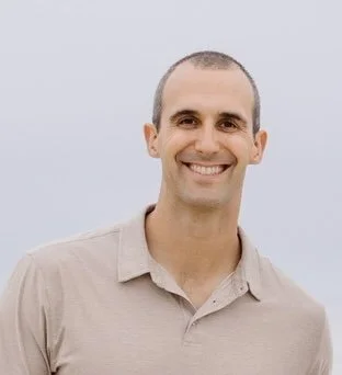 A smiling man with short hair wearing a beige polo shirt, standing outdoors with a neutral background.