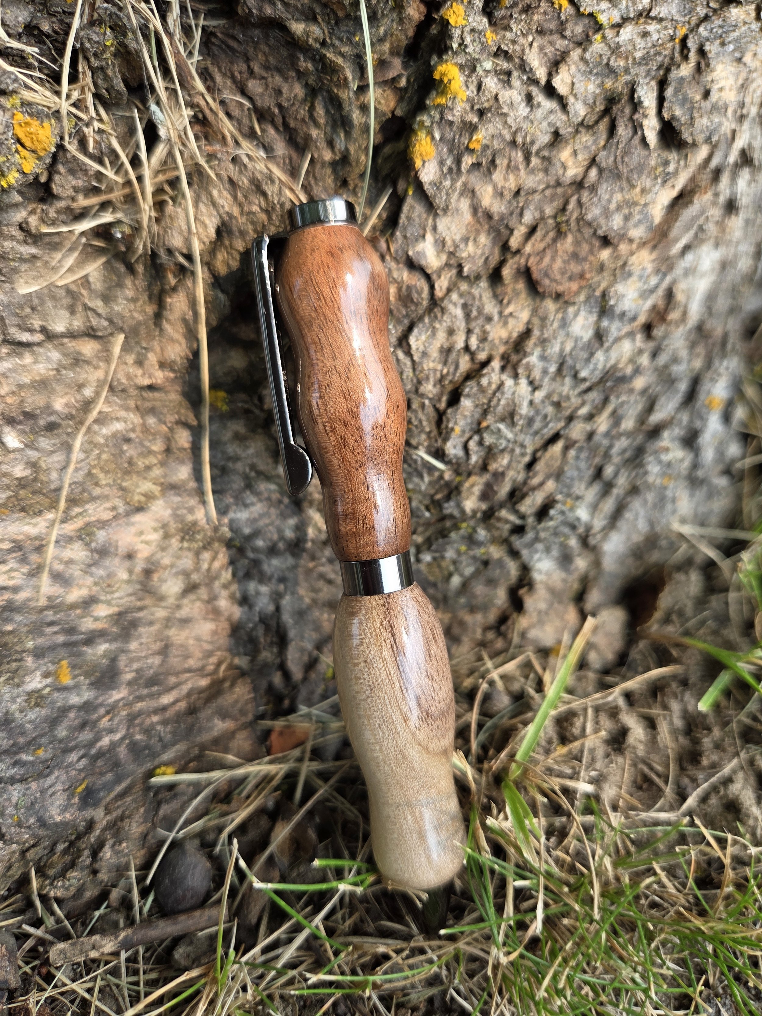 a handmade turned pen made from wood against a tree