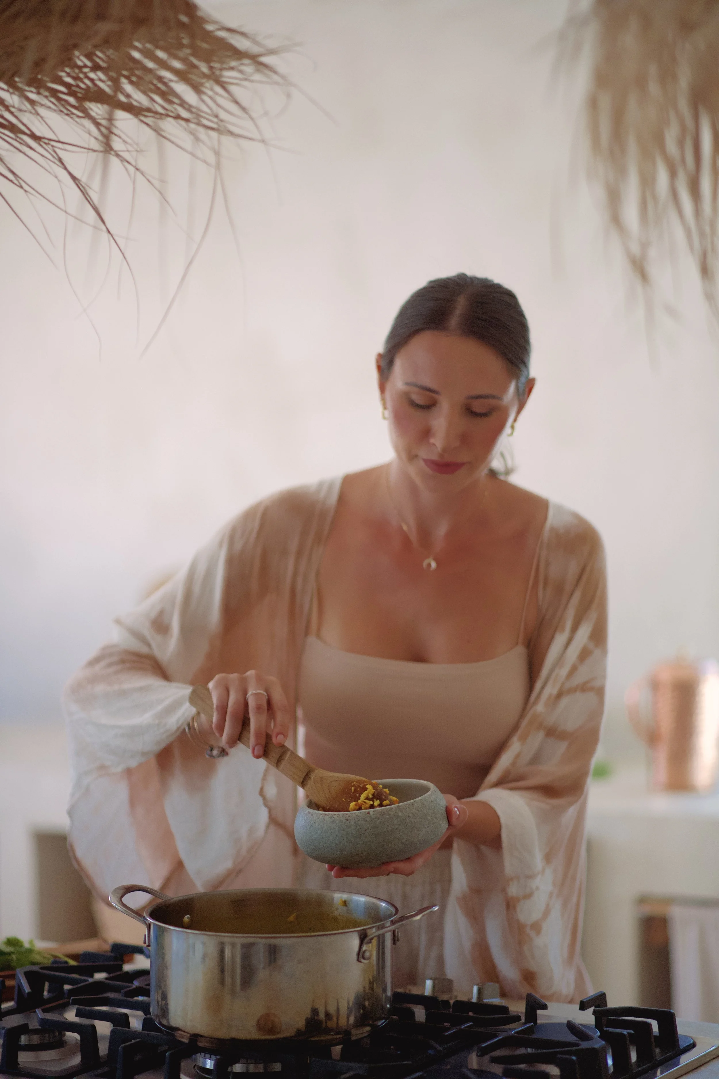 A woman cooking in a modern kitchen, pouring cooked food from a gray bowl into a pot on a stove.