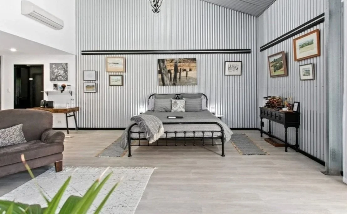 Bedroom with corrugated metal walls and ceiling, black metal bed with gray bedding, framed artwork on the wall, and a chandelier hanging from the ceiling.