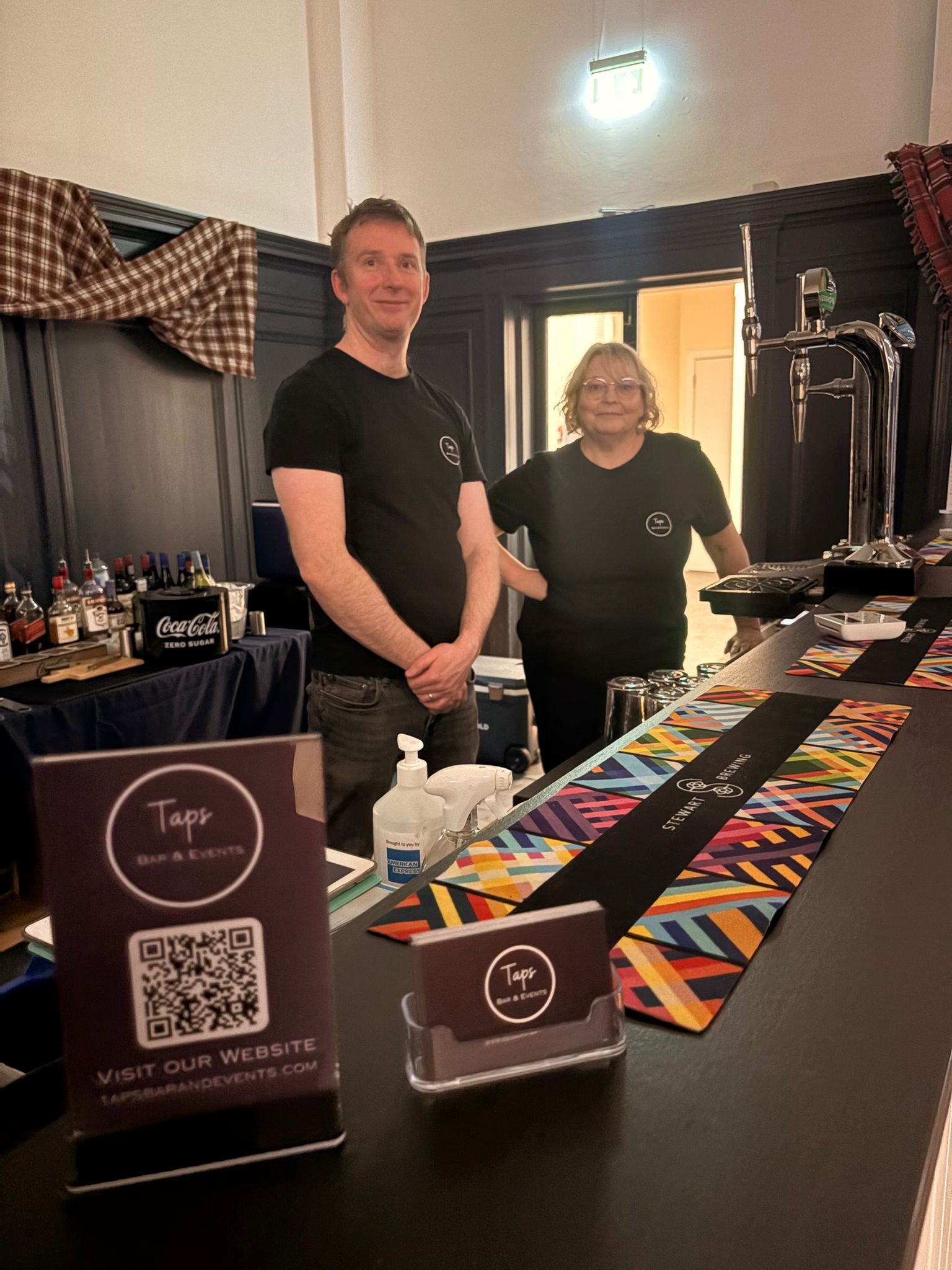 Meet the people behind the taps. Two people standing behind Taps' mobile bar at a Burns Supper event in Edinburgh and Lothians.