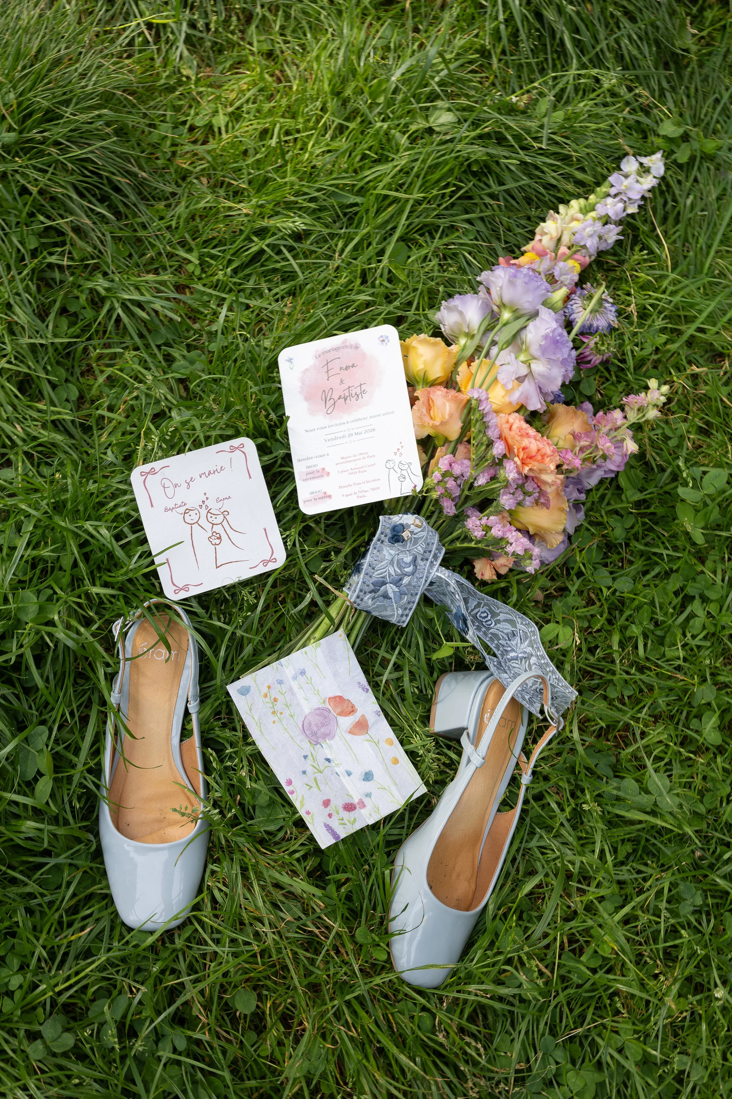 Des escarpins blancs reposant sur de l'herbe verte, entourés de billets et de cartes de vœux pour un mariage.