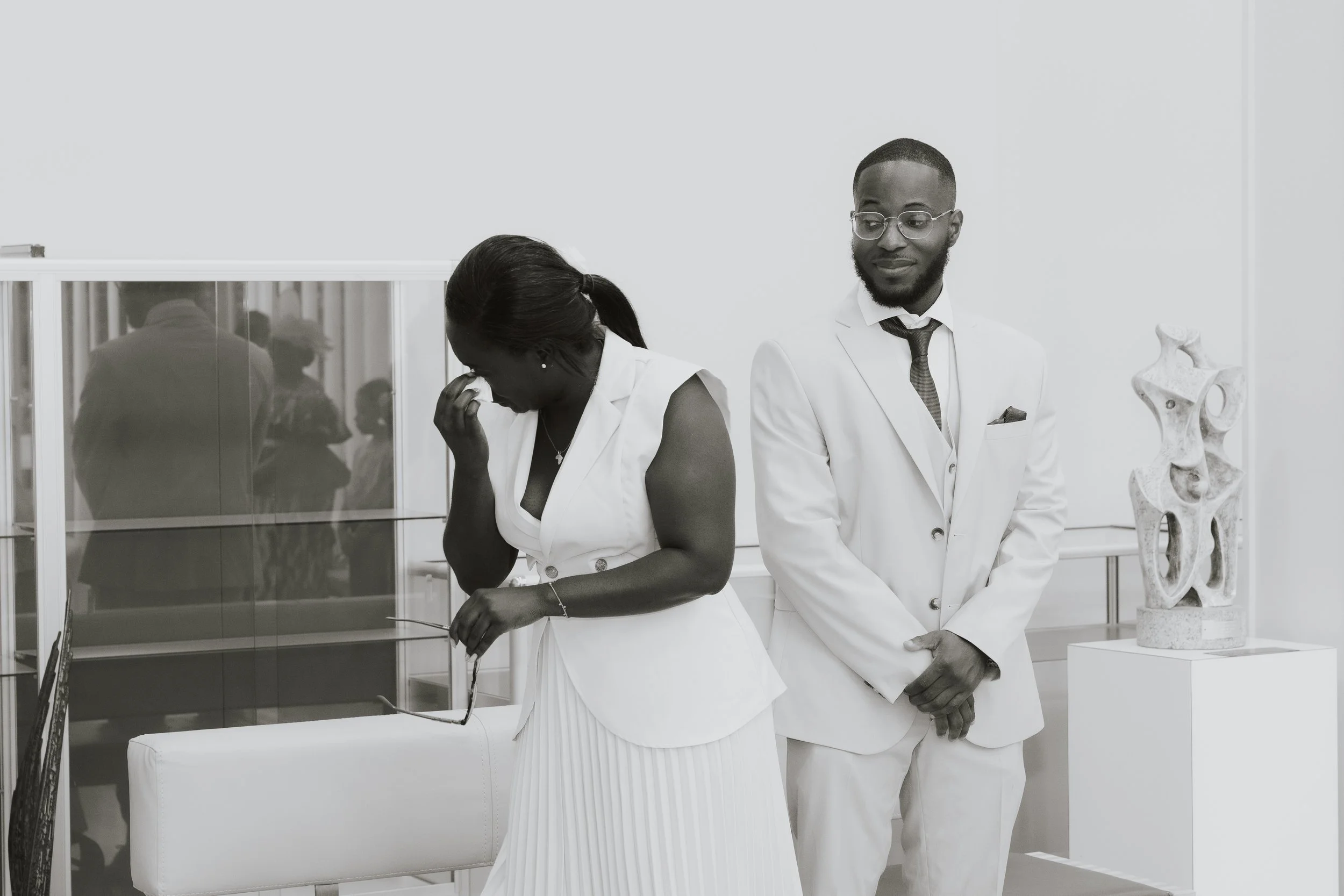 Deux professionnels en tenue blanche, une femme et un homme, dans une pièce d'exposition ou un musée, avec une sculpture moderne en pierre à côté d'eux.