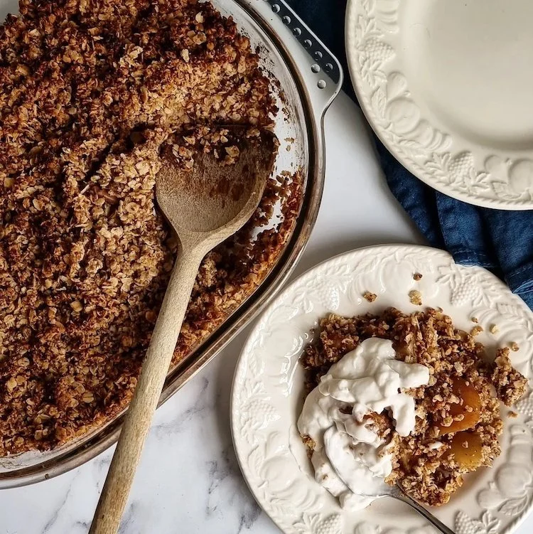 An apple and pear crumble being served onto cream plates