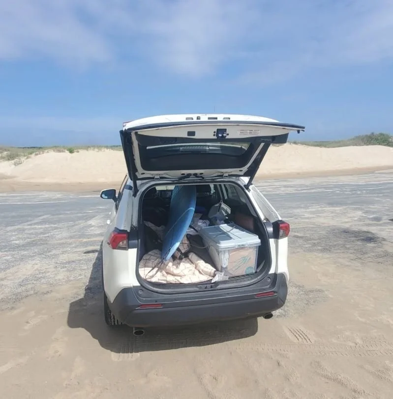 rav4 packed up with surfboard and other camping gear in sandy parking lot at the beach.JPG