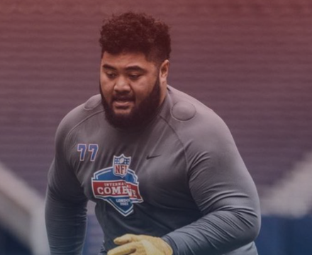 Football player during an indoor practice, wearing a gray practice jersey and gloves.