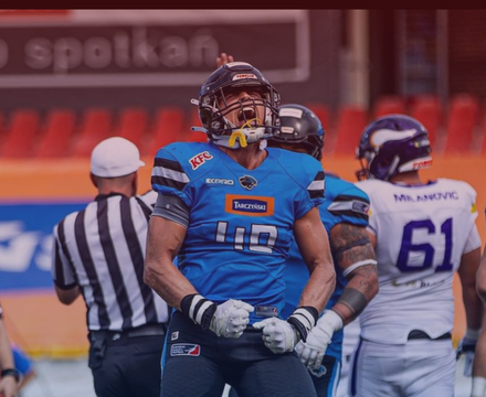 Football player in blue uniform with the number 10, wearing a helmet and gloves, celebrating on the field with teammates and a referee nearby.