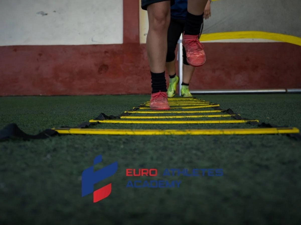 People running through agility ladder training on indoor turf, with 'EURO ATHLETES ACADEMY' logo visible on the ground.