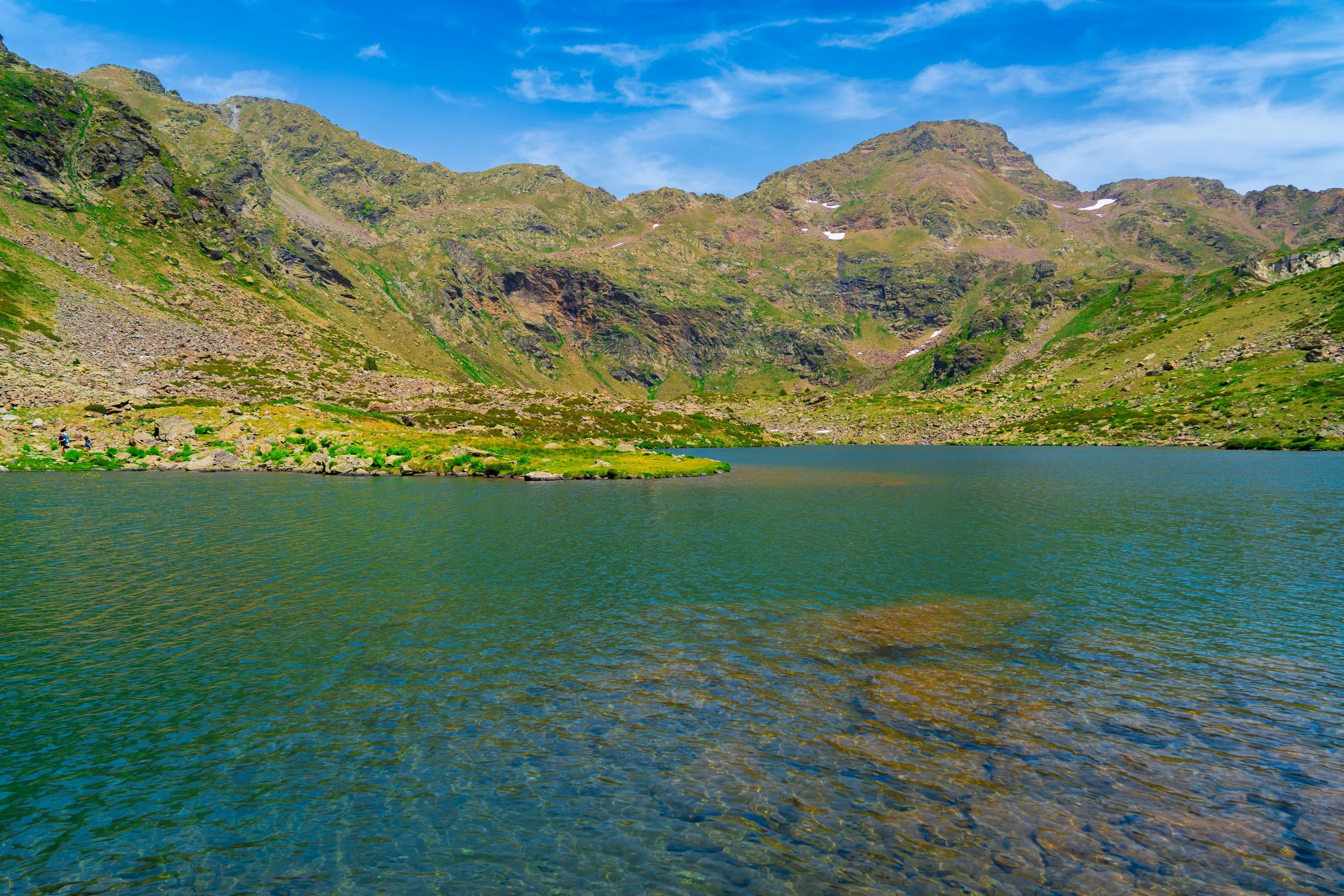 Paisaje de montaña con lago en primer plano y cielo azul con nubes