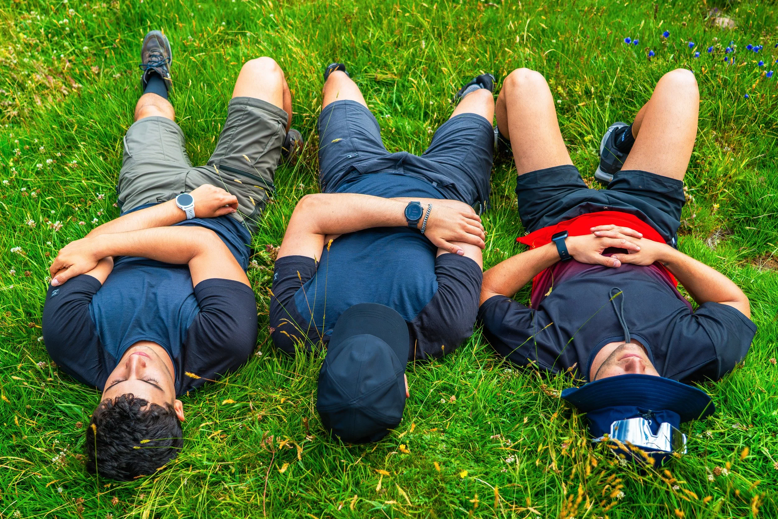 Grupo de cuatro personas acostadas en la hierba de un campo, con ropa deportiva, disfrutando del día al aire libre.