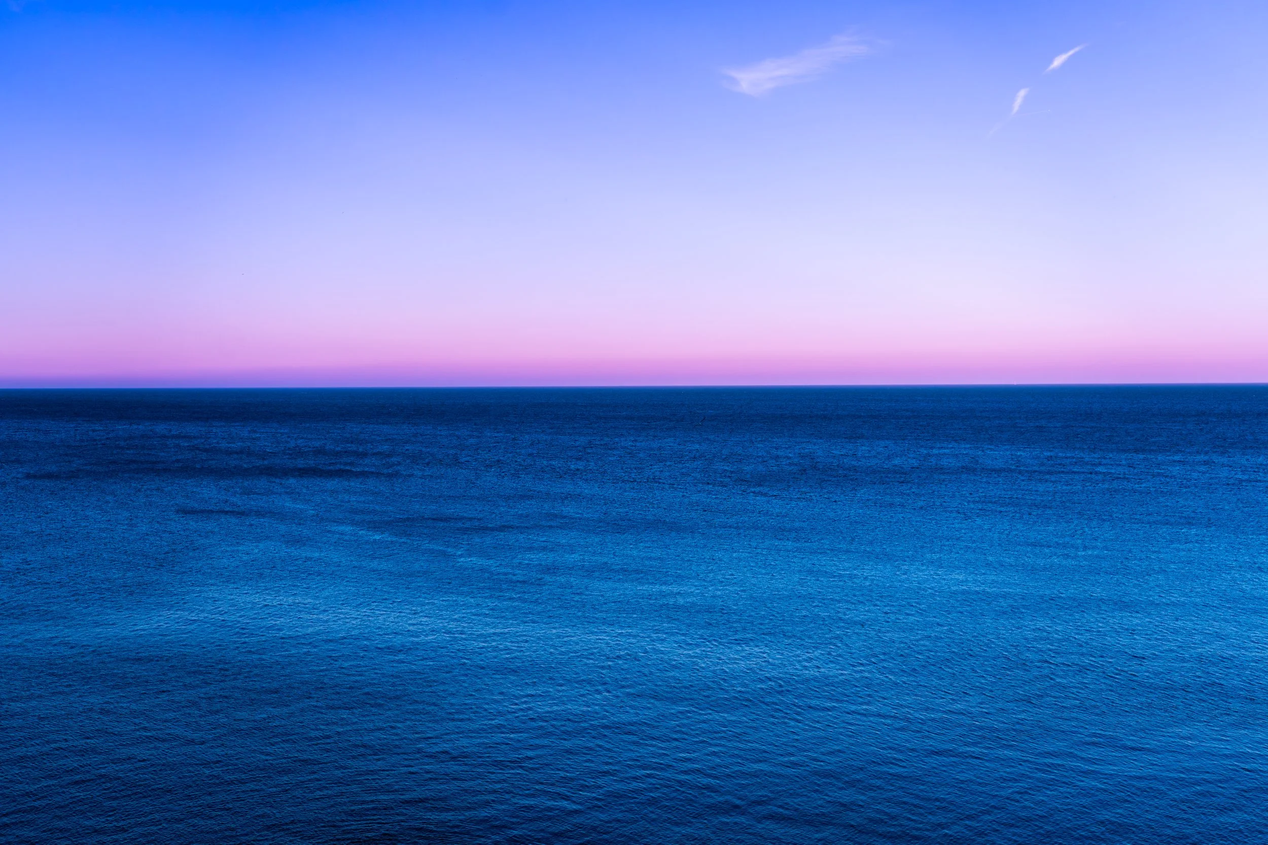 Vista del mar con un cielo azul y tonos rosados en el horizonte, sin elementos adicionales.