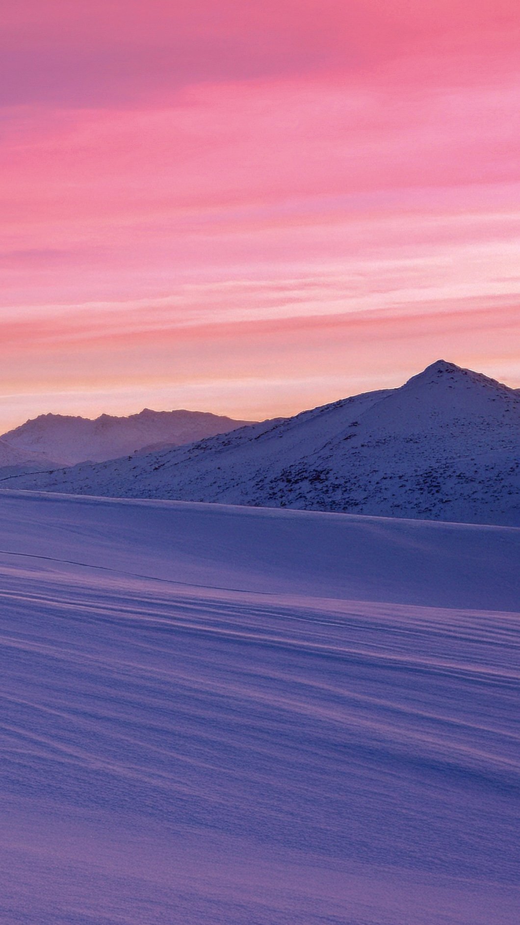 Montañas cubiertas de nieve bajo un cielo con tonos rosados y lilas en el atardecer.