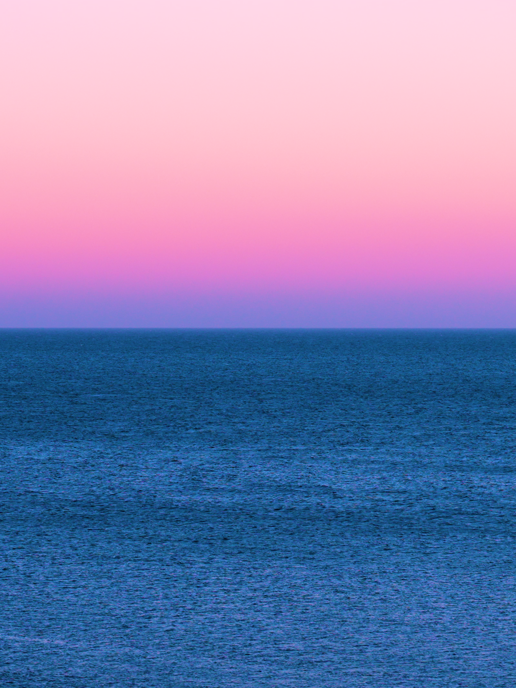 Vista del océano con un cielo rosa y morado en el horizonte.