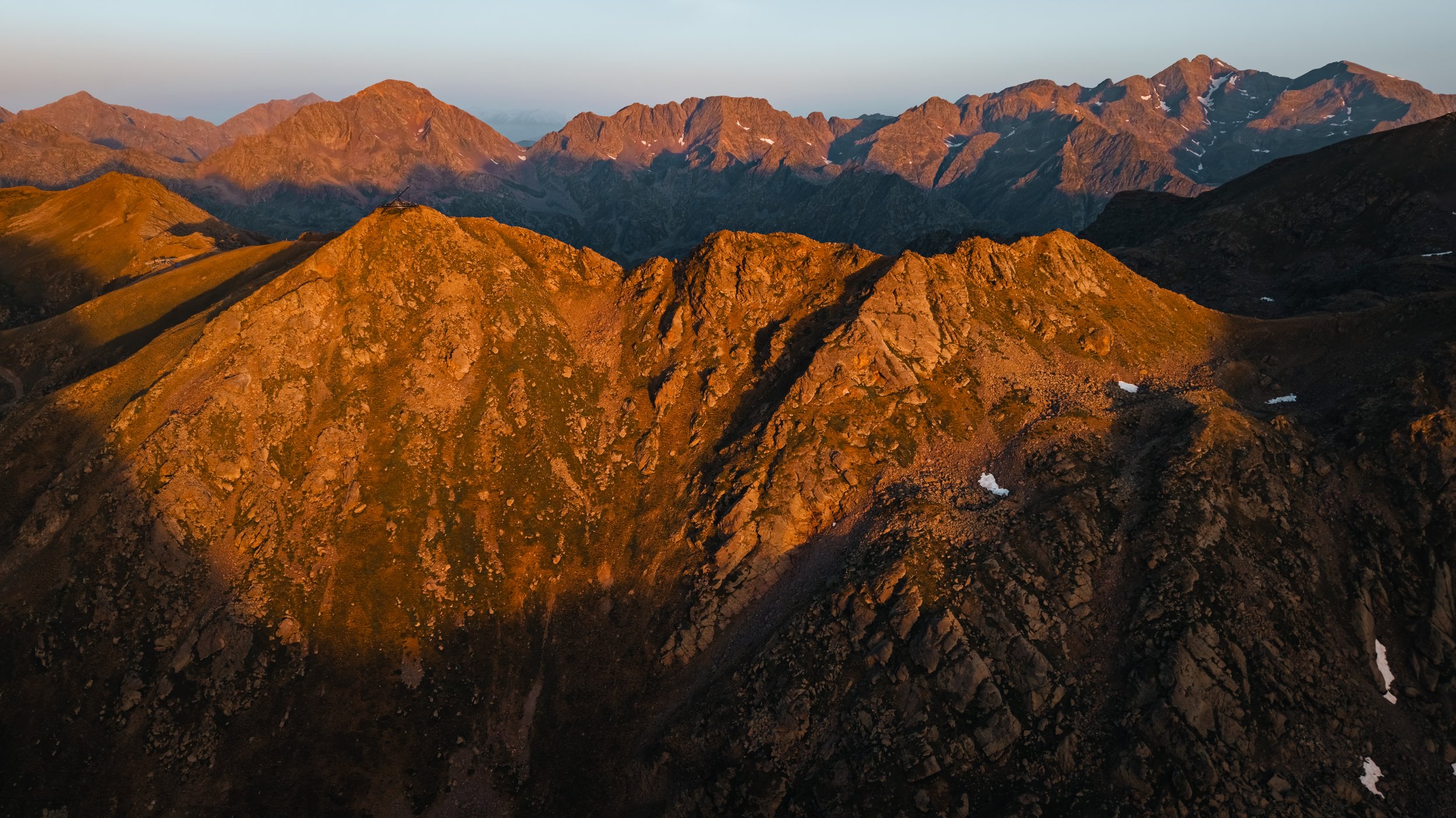 Montañas al atardecer con picos rocosos y algunos restos de nieve en las cumbres.