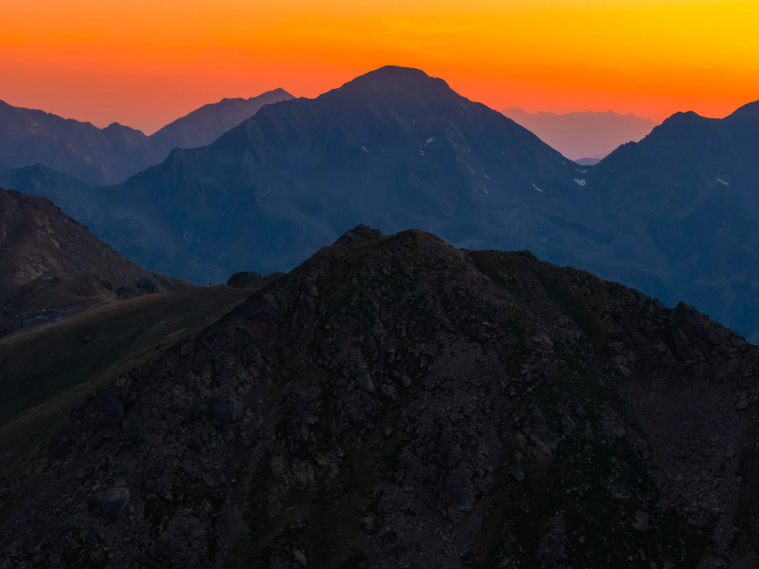 Montañas durante un atardecer con el cielo en tonos anaranjados y rojos, y cumbres cubiertas parcialmente con nieve.