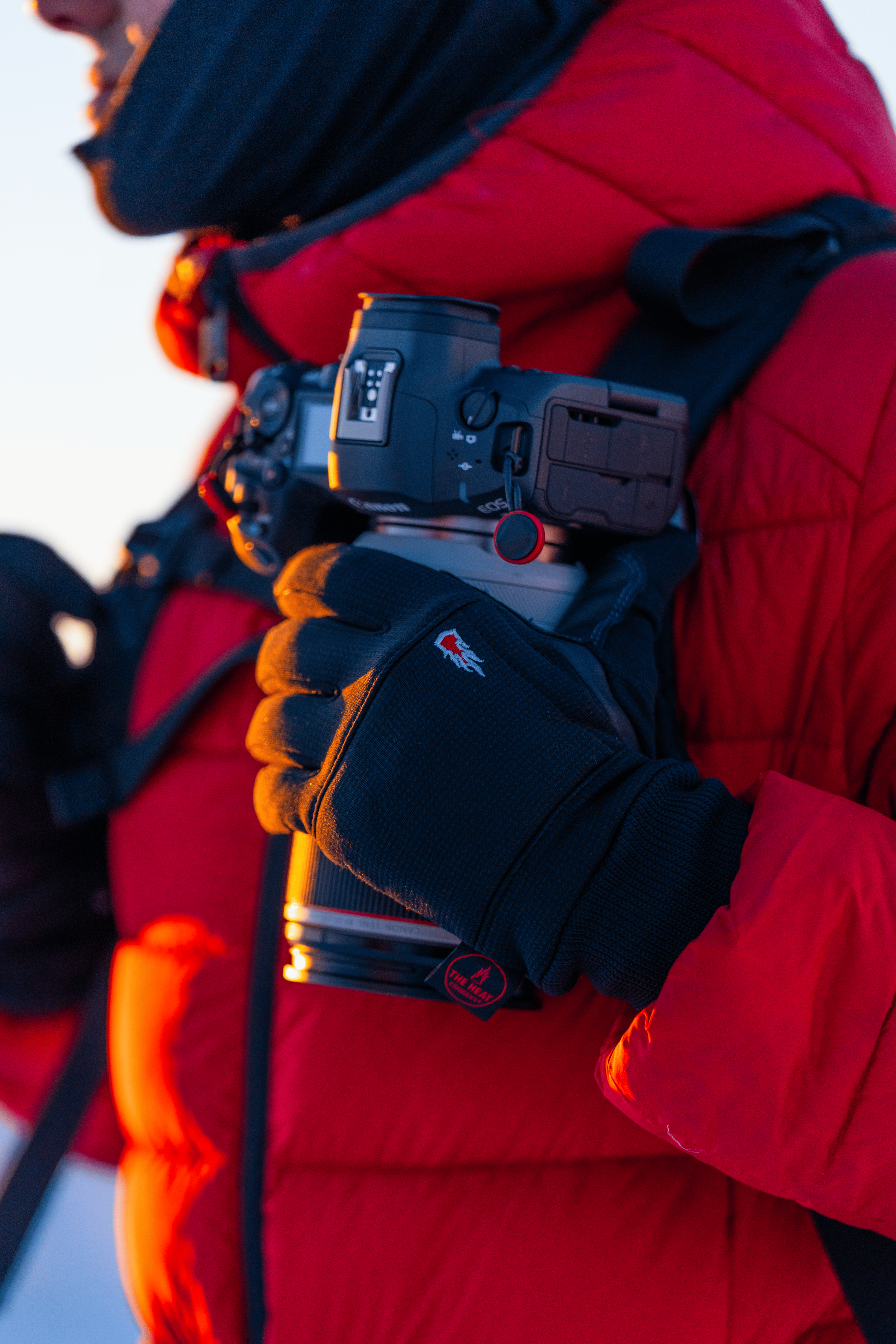 Persona con ropa de abrigo roja y guantes negros, sosteniendo una cámara réflex en un entorno exterior.
