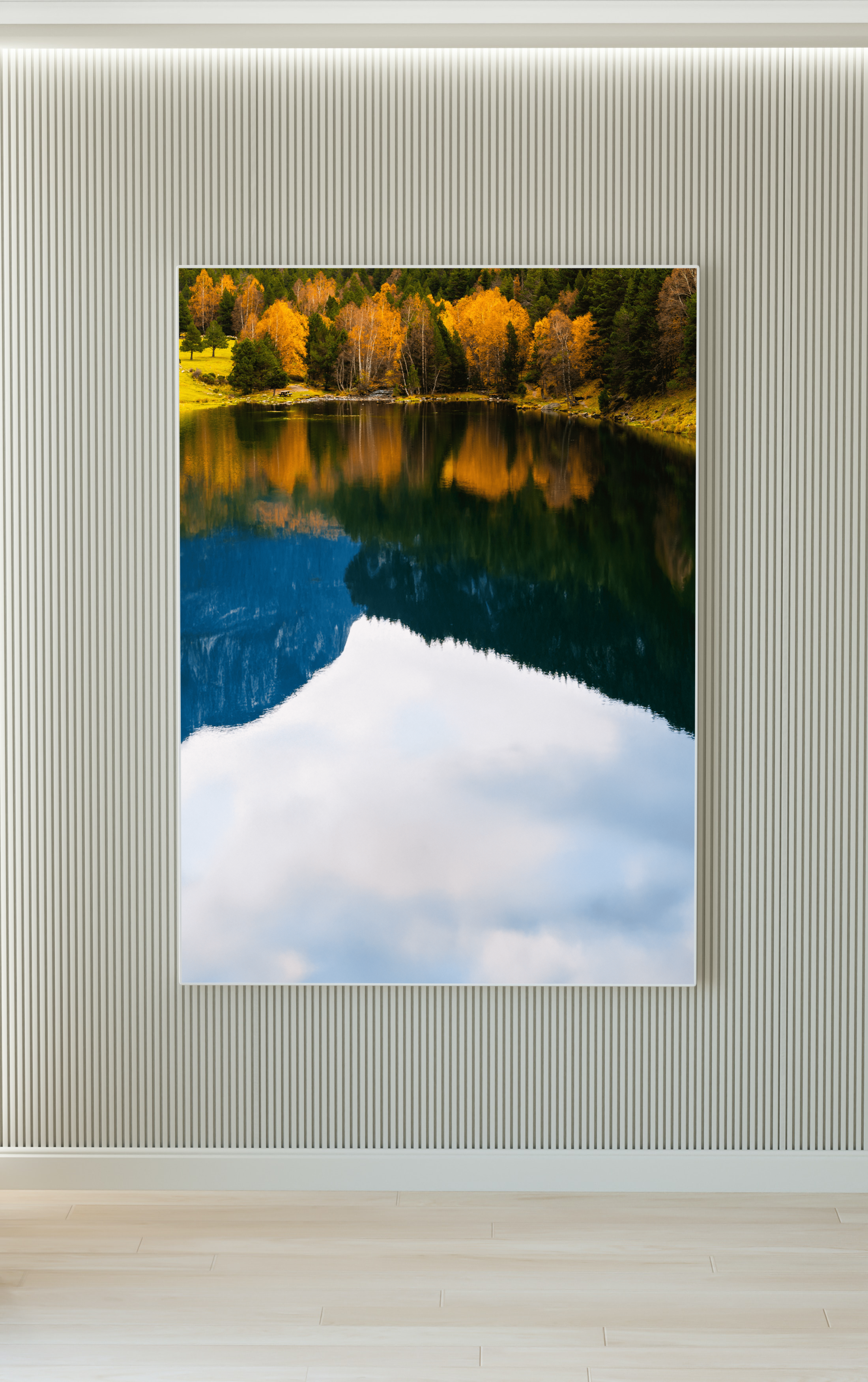 Cuadro con paisaje de árboles otoñales junto a un lago y montañas reflejadas en el agua, en una pared de interior