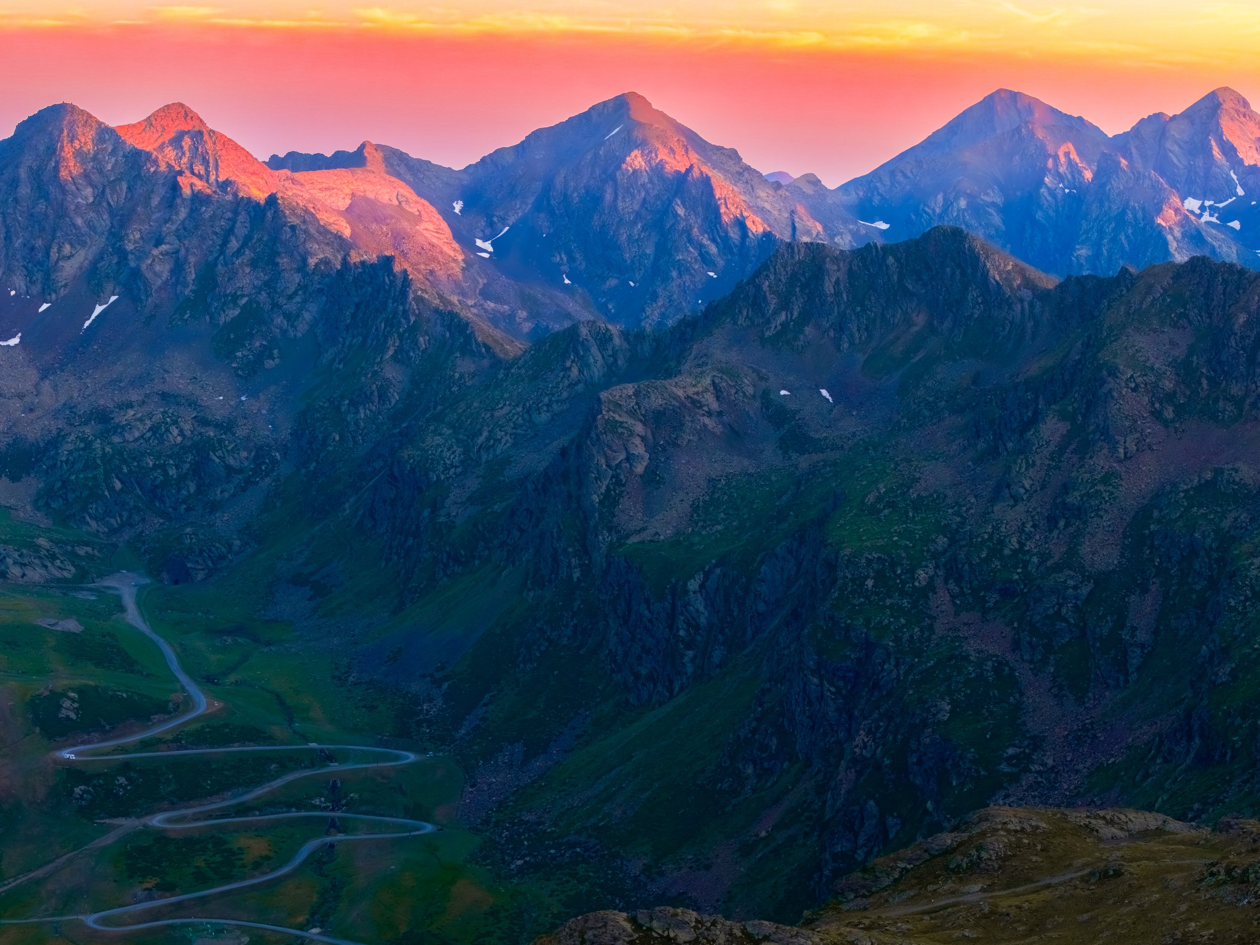 Montañas con picos rojos y azules, con un cielo colorido y caminos en la parte inferior.