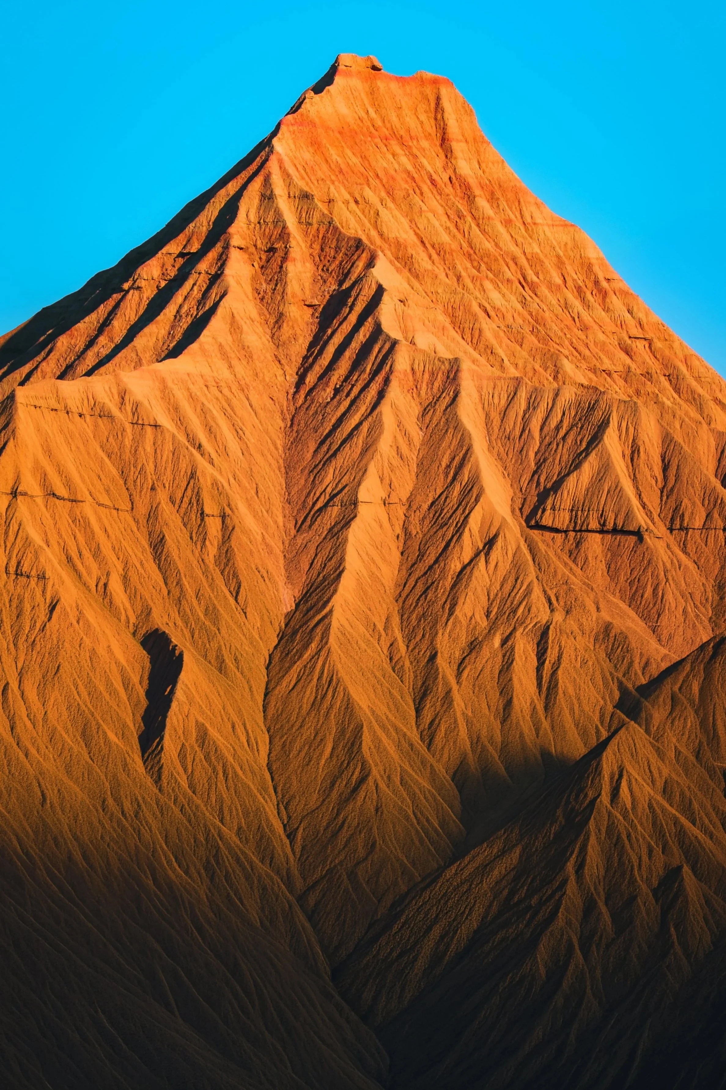 Montaña con picos afilados y estriados en tonos naranjas y oscuros, bajo un cielo azul claro.