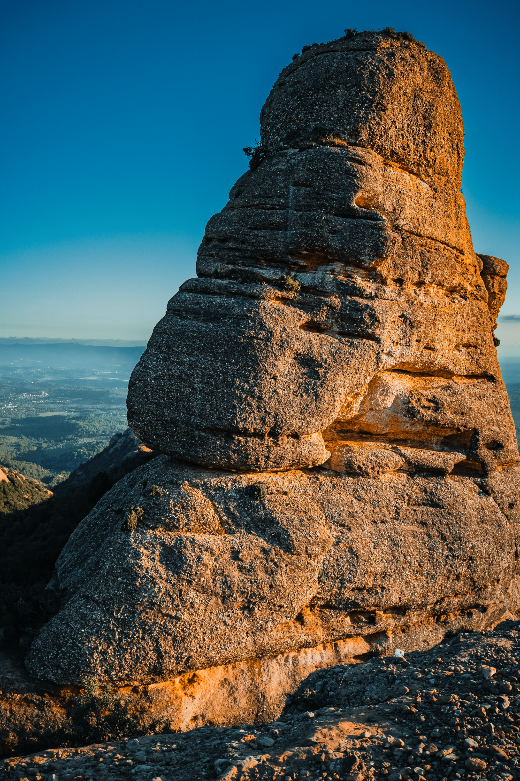 Formaciones rocosas en la cima de una montaña al atardecer, con un cielo despejado y un paisaje de valle en el fondo.