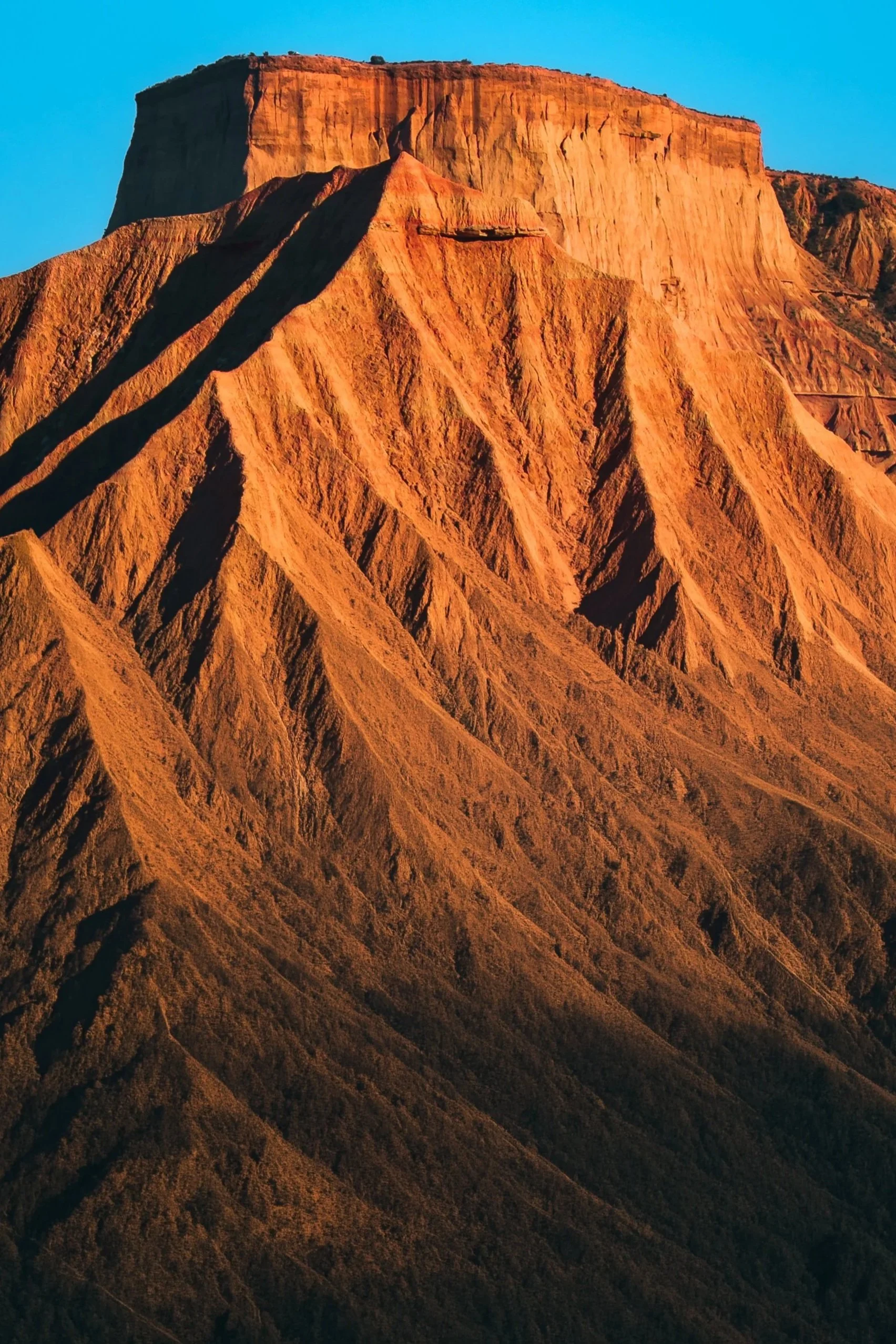 Montaña de color rojizo con pendientes escarpadas, bajo cielo azul claro.