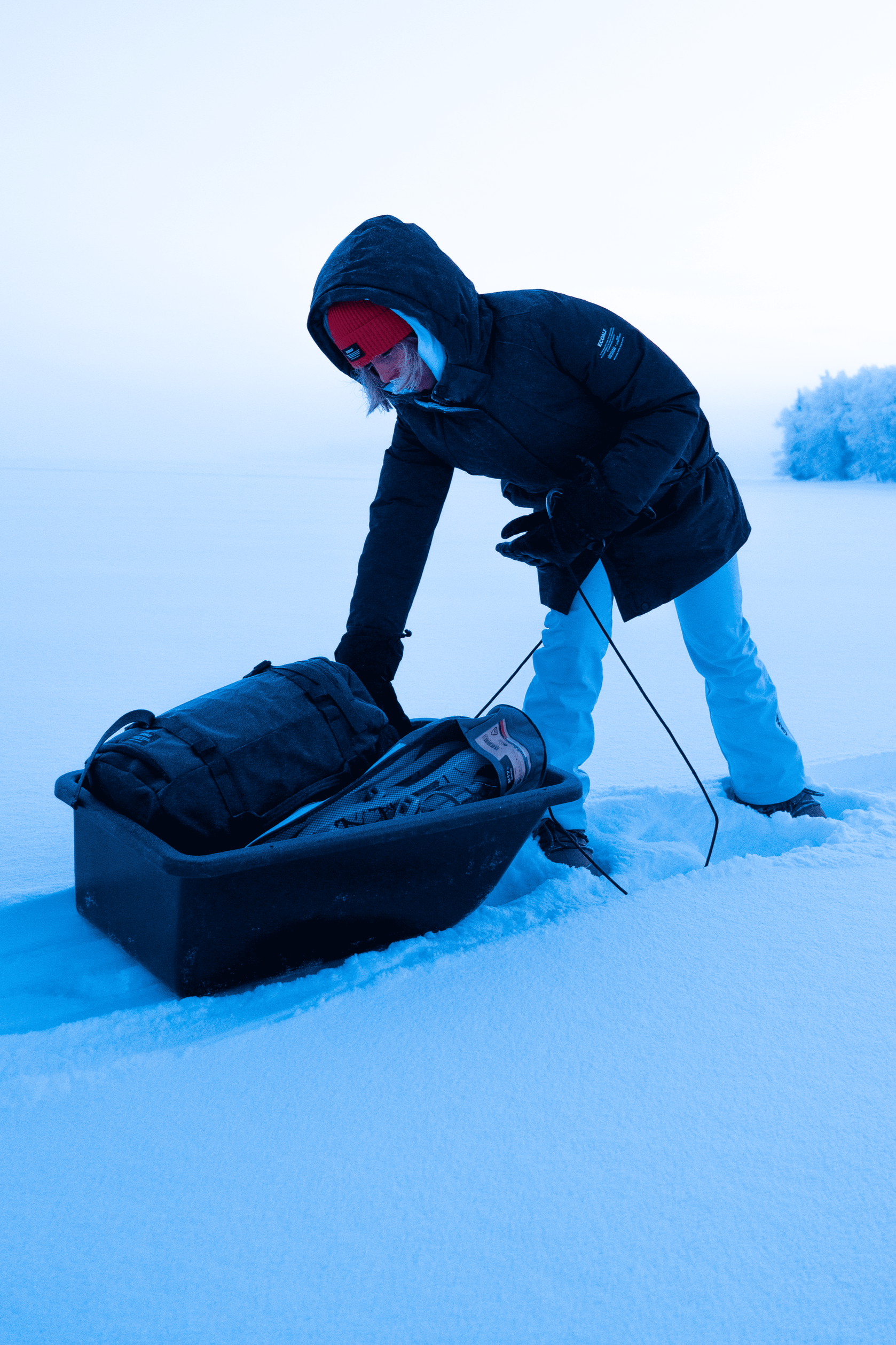 Persona en la nieve, colocando una mochila en un trineo en un paisaje invernal.