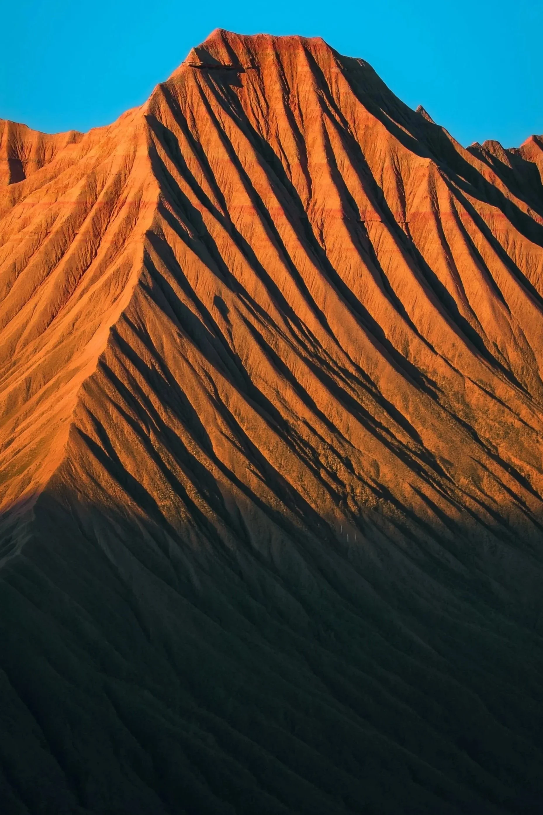 Montaña con estrías rojas y oscuras bajo un cielo azul claro.
