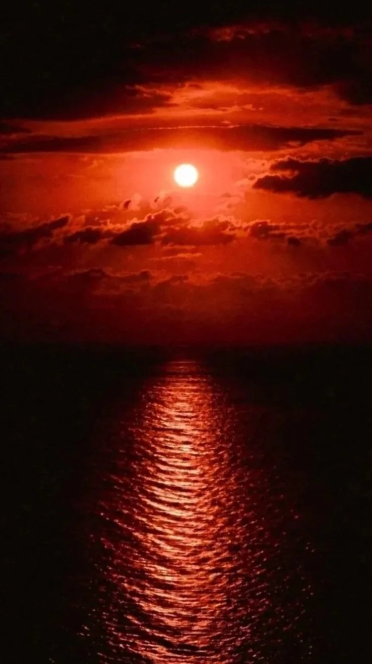 Atardecer con el sol brillante sobre el mar y nubes oscuras en el cielo, reflejándose en el agua.