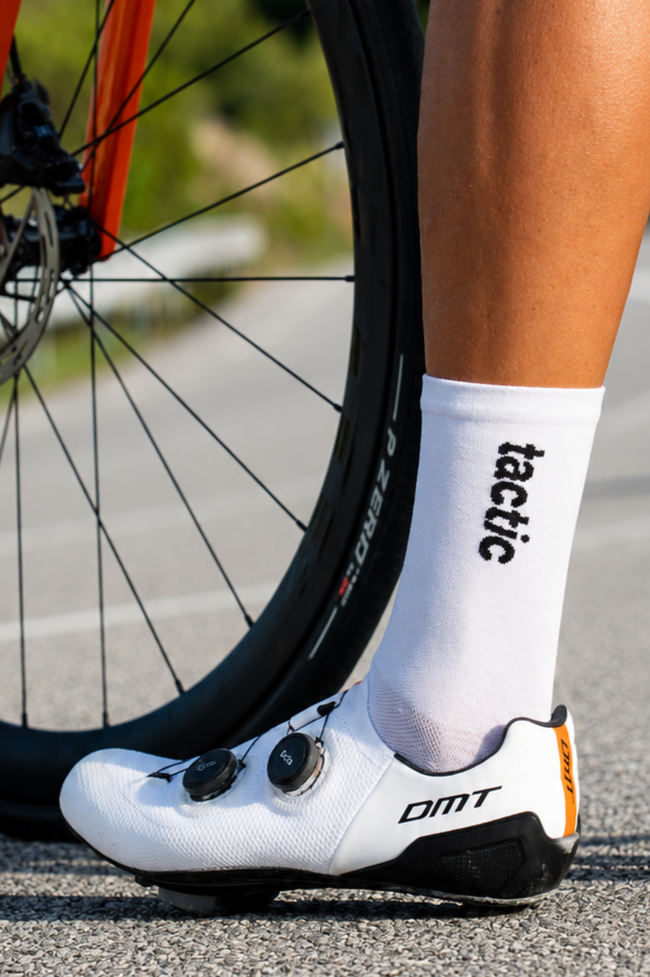 Pie de atleta con calzado de ciclismo y calcetines blancos en un camino pavimentado.