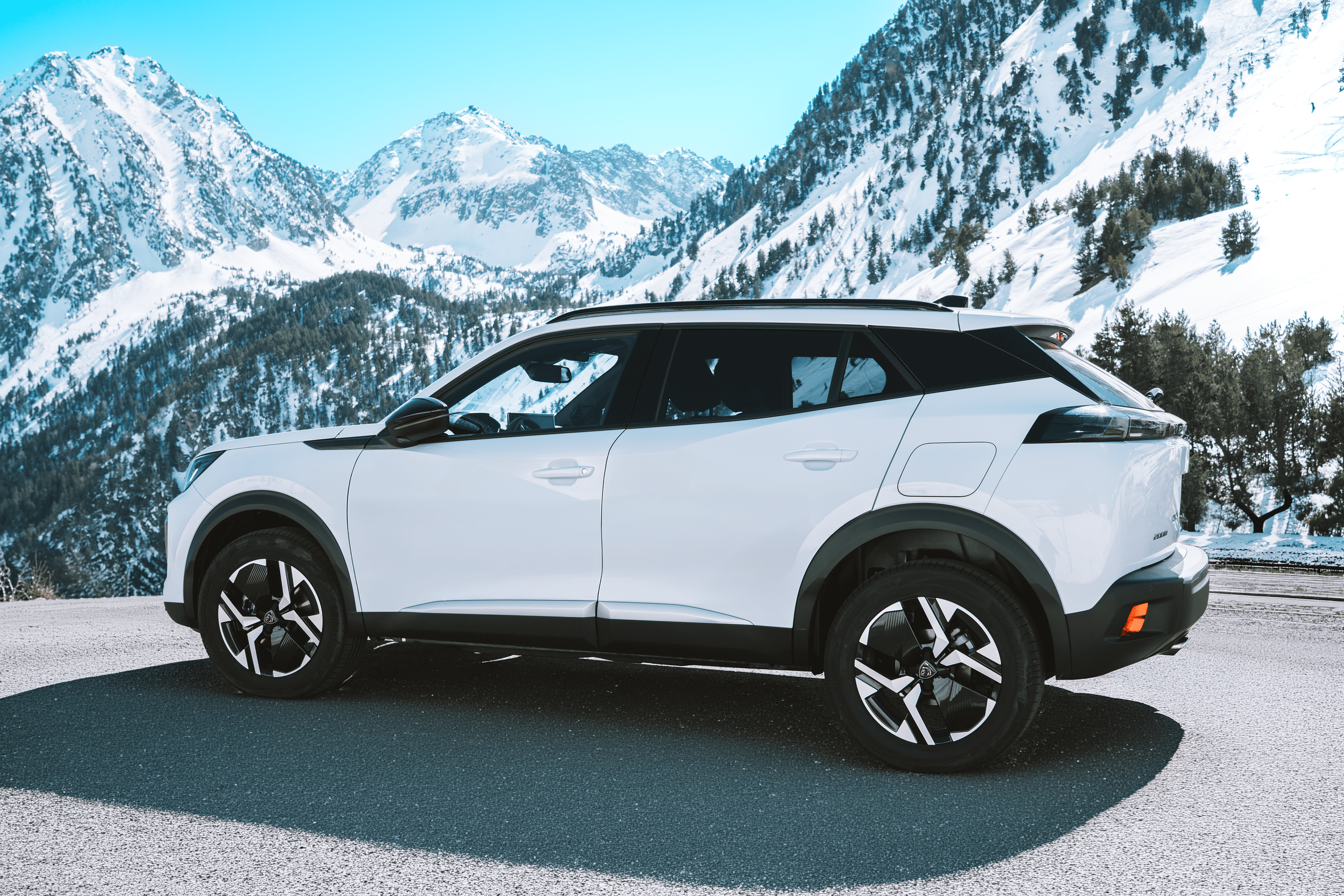 Coches blancos estacionados en un paisaje de montañas nevadas y árboles en un día soleado.