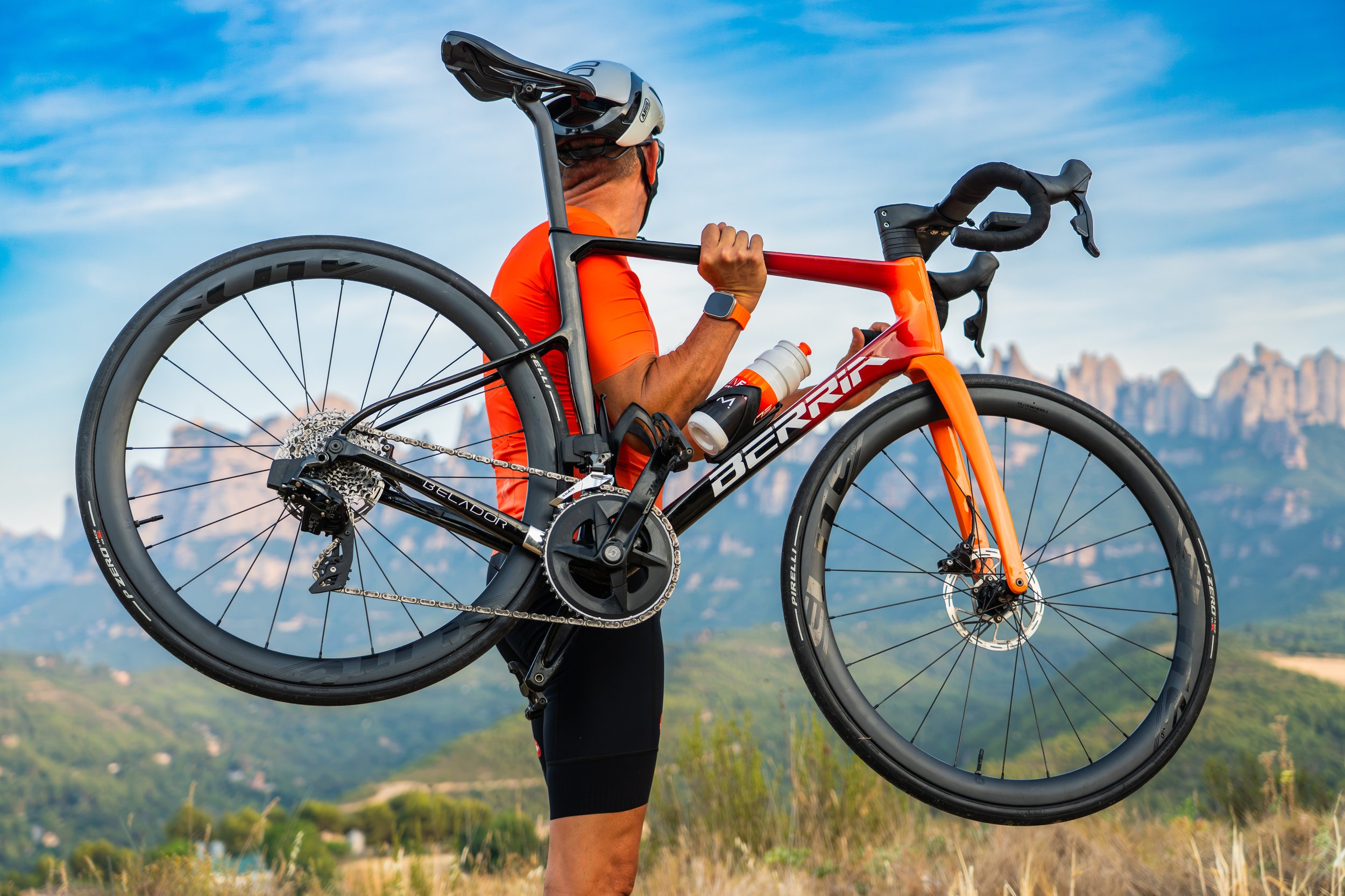 Persona llevándose una bicicleta de ruta en un paisaje montañoso con cielo despejado.