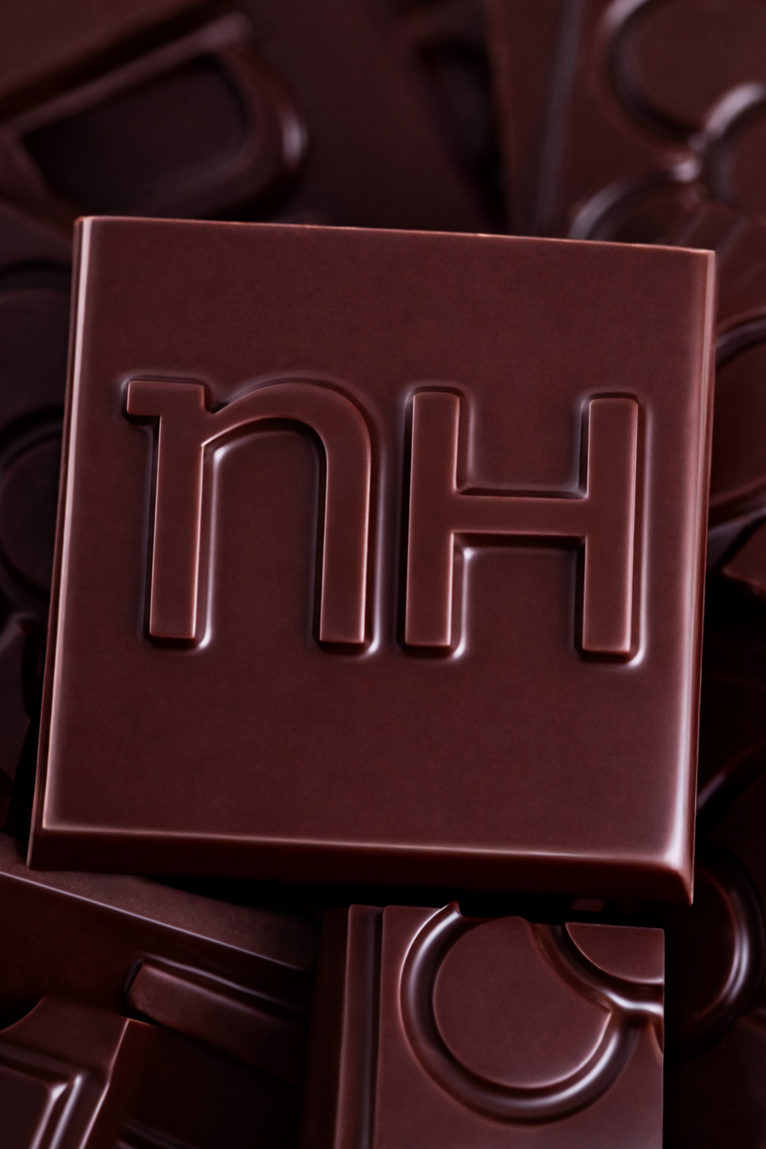 Caja de chocolates de color marrón oscuro con el logo 'nh' en relieve en el centro.