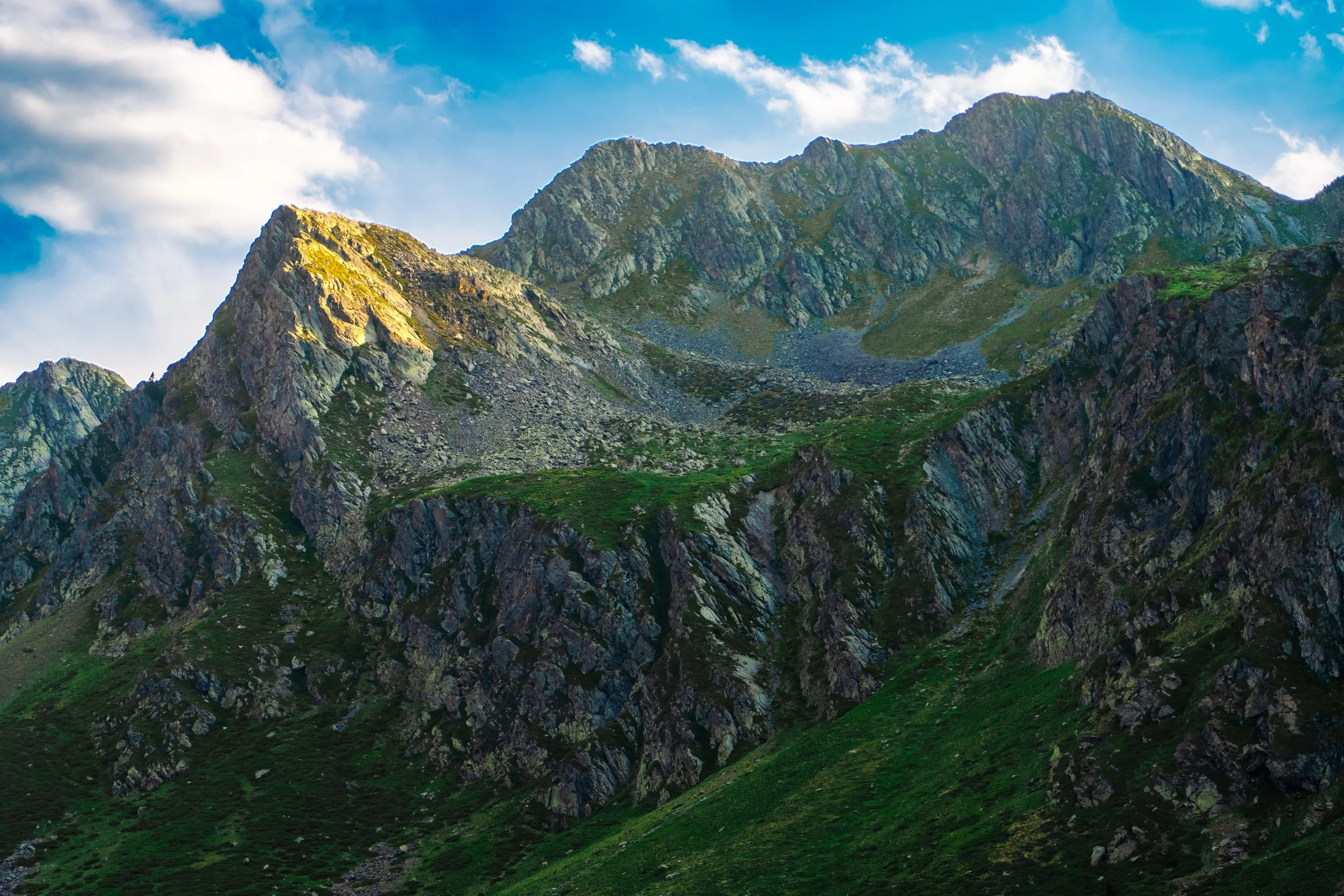 Montañas rocosas con vegetación verde, cielo con nubes.