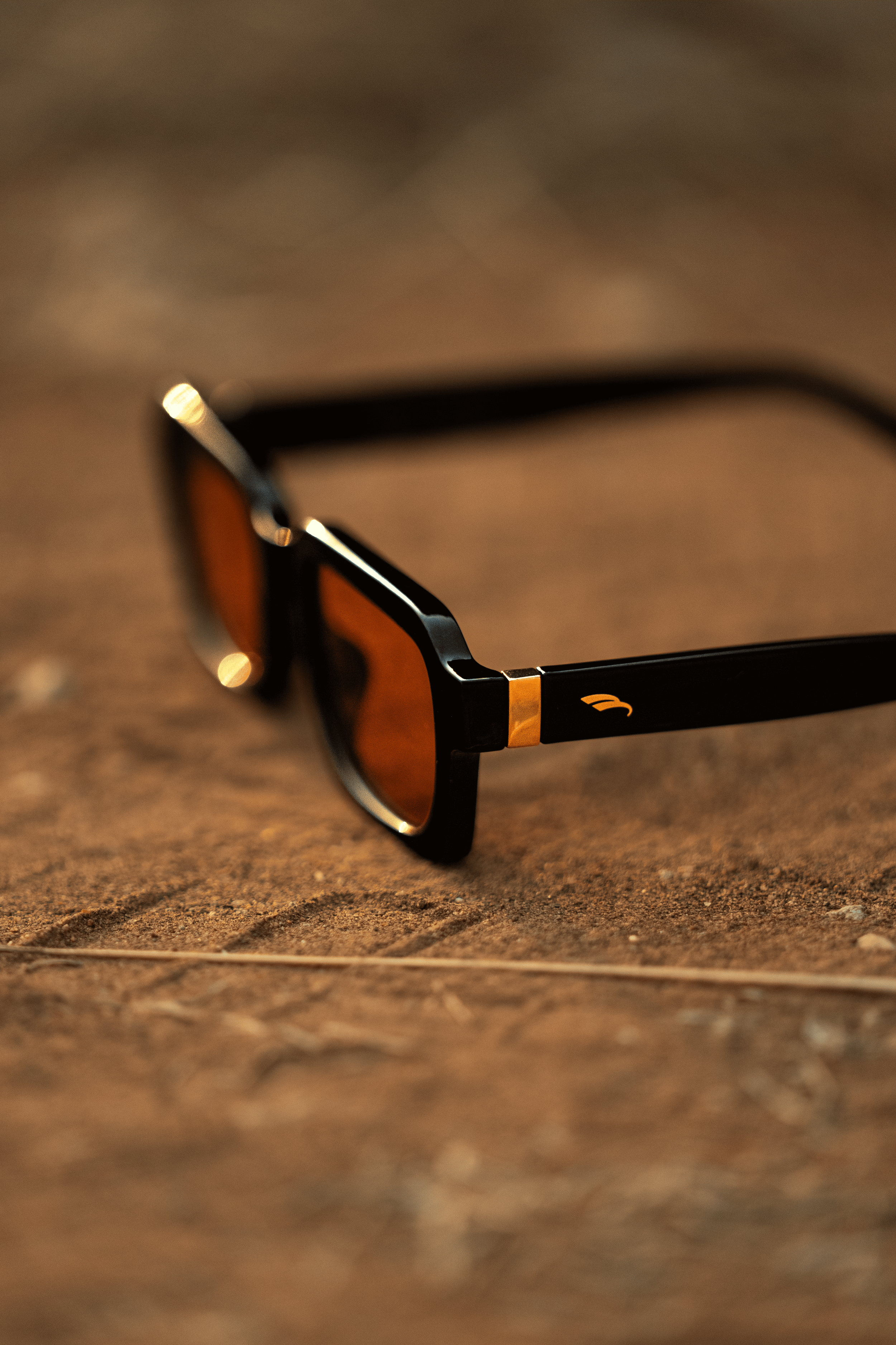 Gafas de sol con marco negro y lentes ámbar, descansando sobre una superficie de madera.