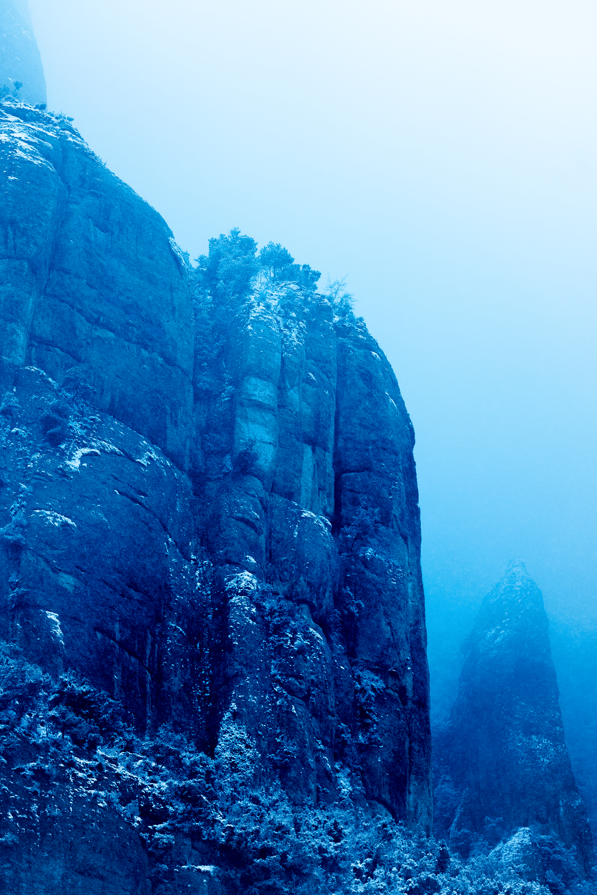 Acantilados de roca con nieve en un paisaje montañoso, rodeados de niebla.
