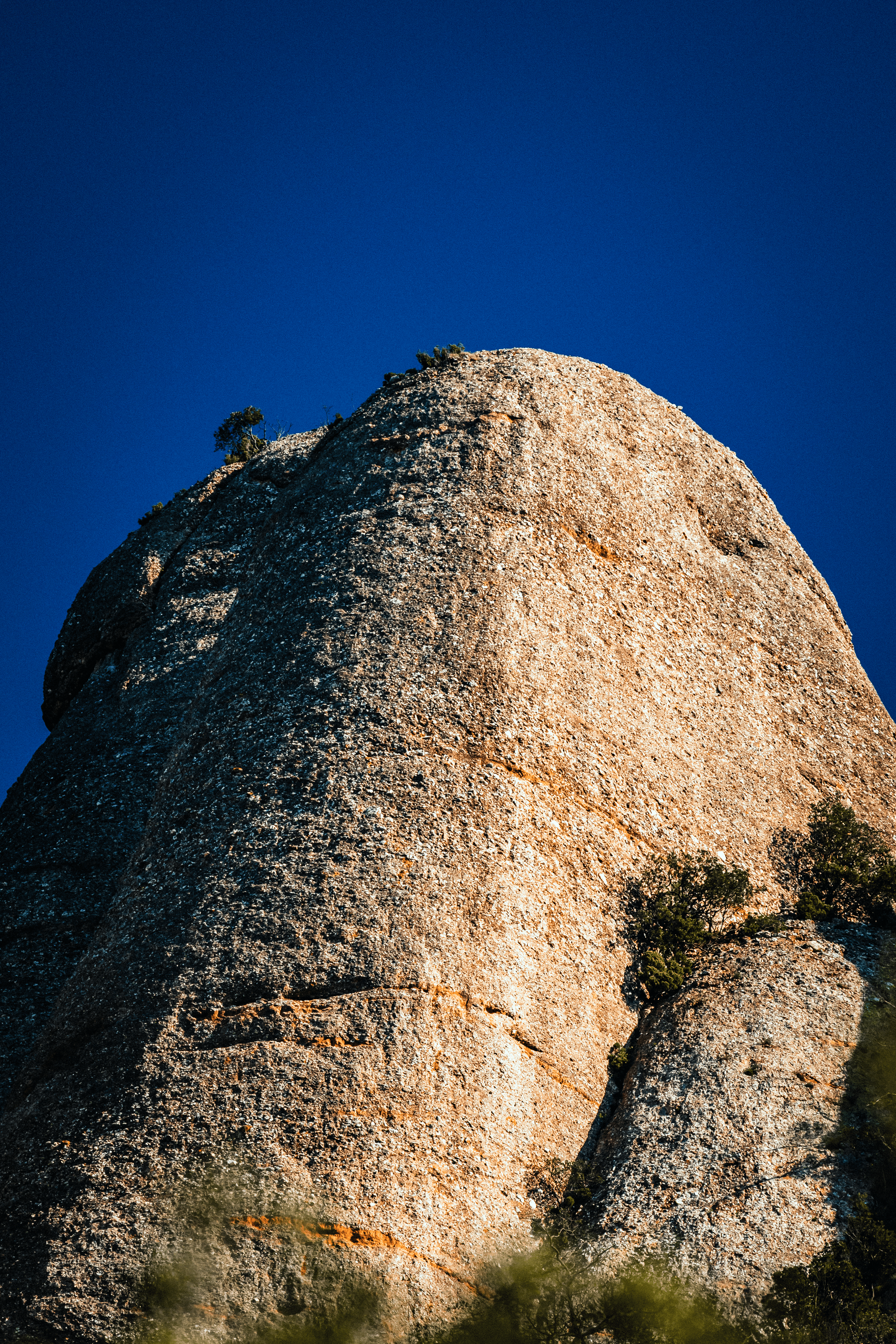 Una gran roca de granito con un cielo azul de fondo y algunos árboles pequeños alrededor.