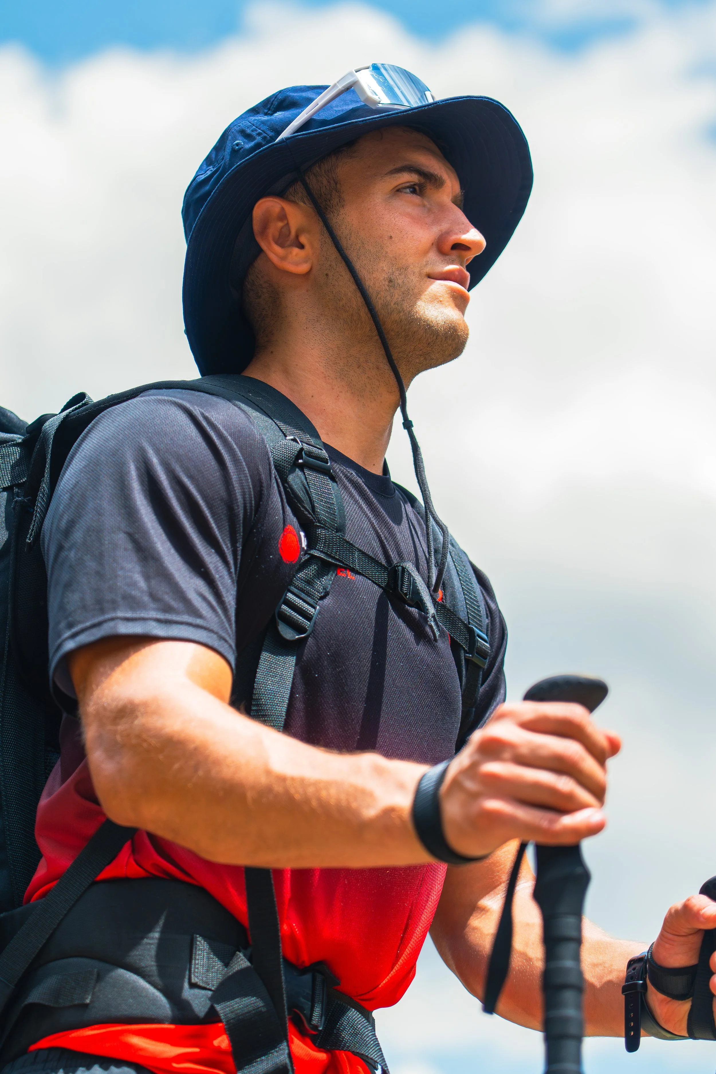 Joven hombre haciendo running, lleva gorra, audífonos, mochila y ropa deportiva, sostiene un dispositivo móvil en la mano.