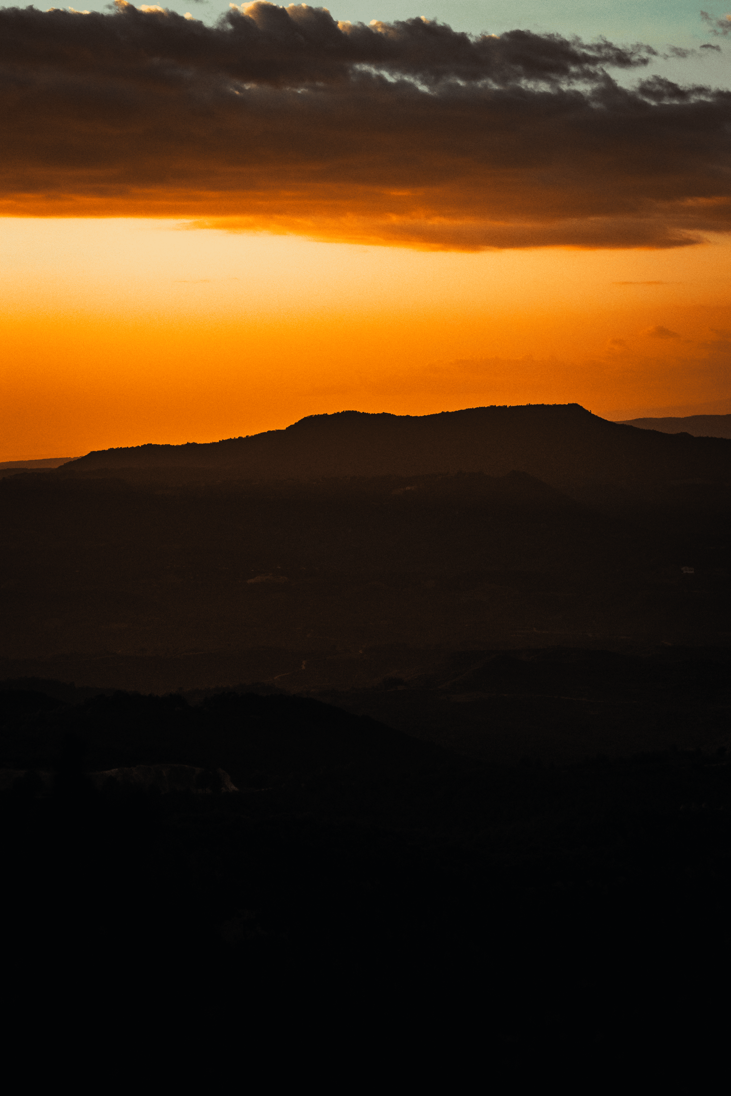 Atardecer con nubes oscuras sobre cerros y montañas en el horizonte