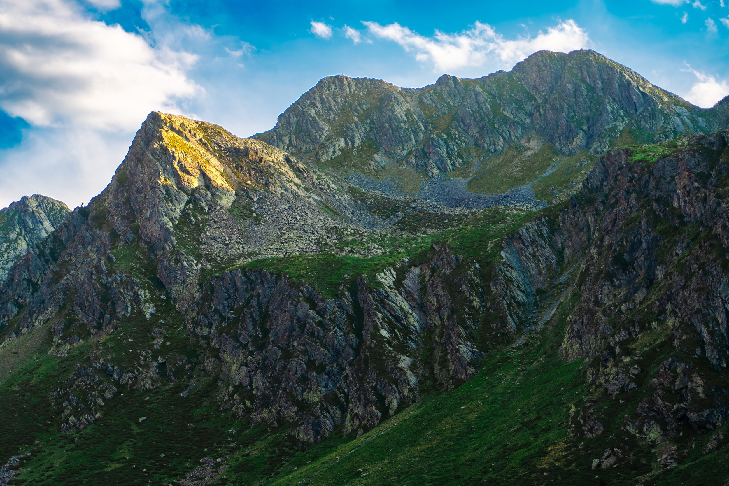 Montañas rocosas con vetas verdes y cielo con nubes dispersas.
