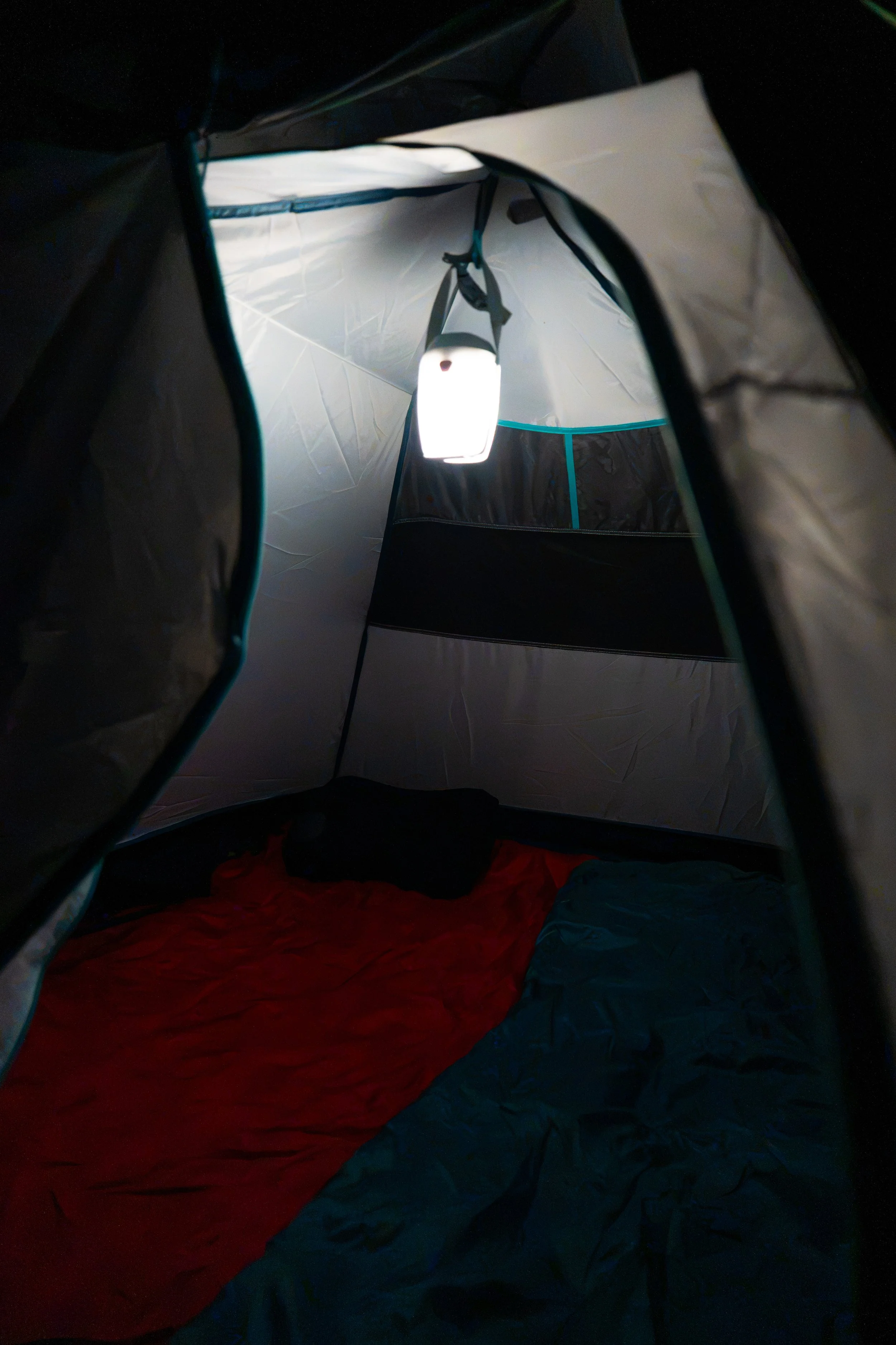 Vista interior de una tienda de campaña con luz apagada y saco de dormir rojo en el suelo.