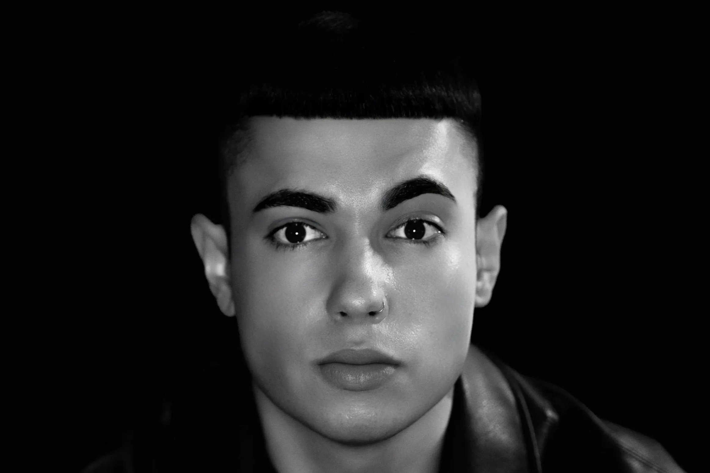 Retrato en blanco y negro de una mujer con cabello corto y cejas oscum azul oscuro, usando una chaqueta de cuero, frente a un fondo negro.