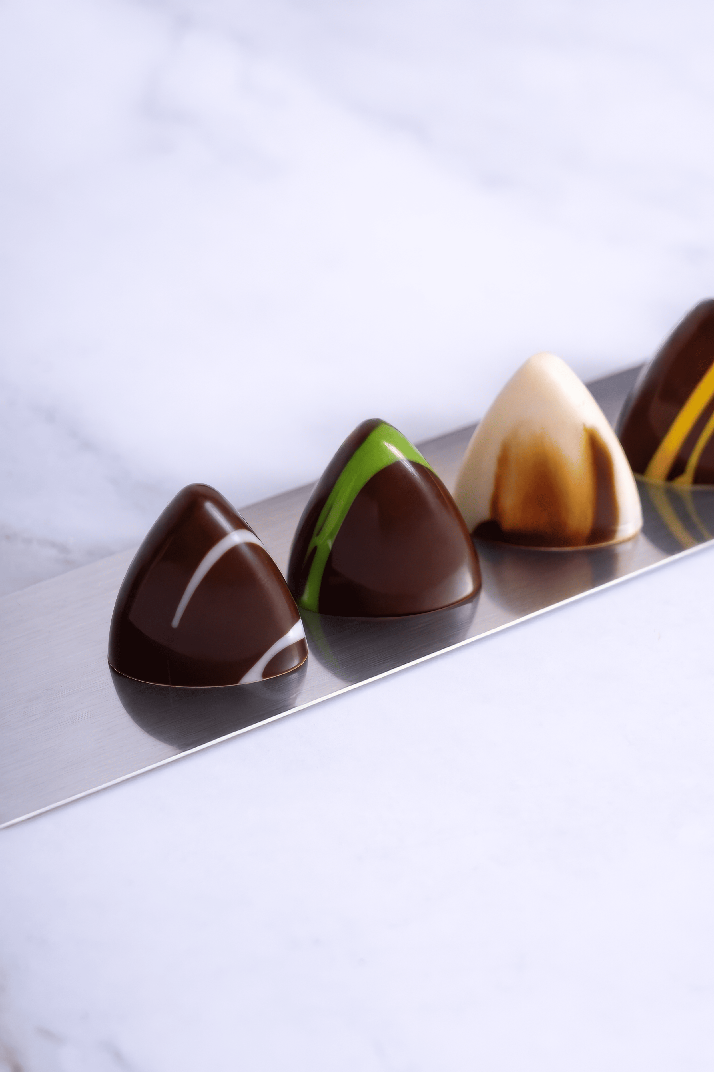 Cuatro chocolates artesanales decorados con diferentes coberturas y colores, colocados en una bandeja de metal.