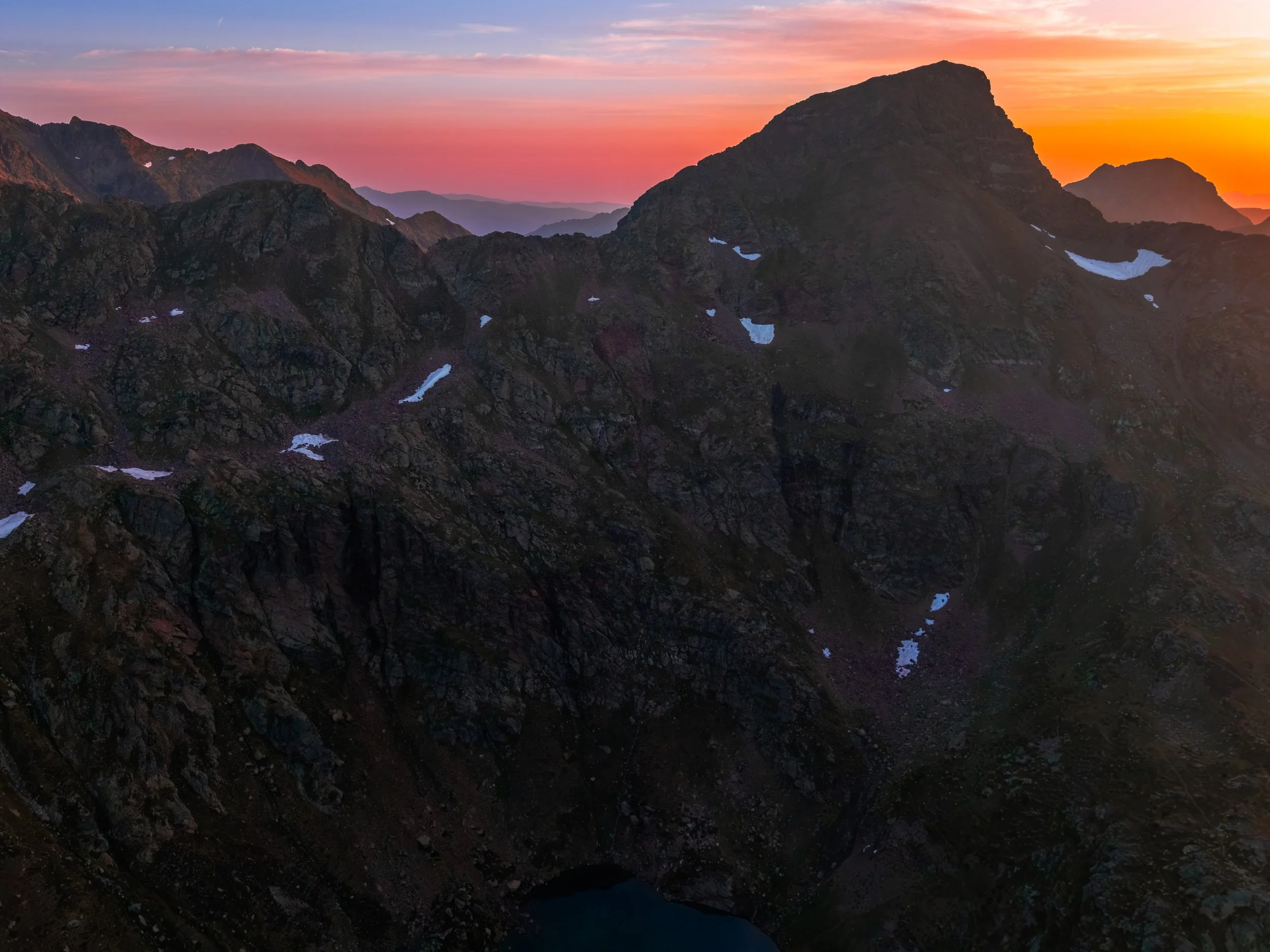 Montañas rocosas y desnudas al atardecer con un cielo en tonos rosa, naranja y azul